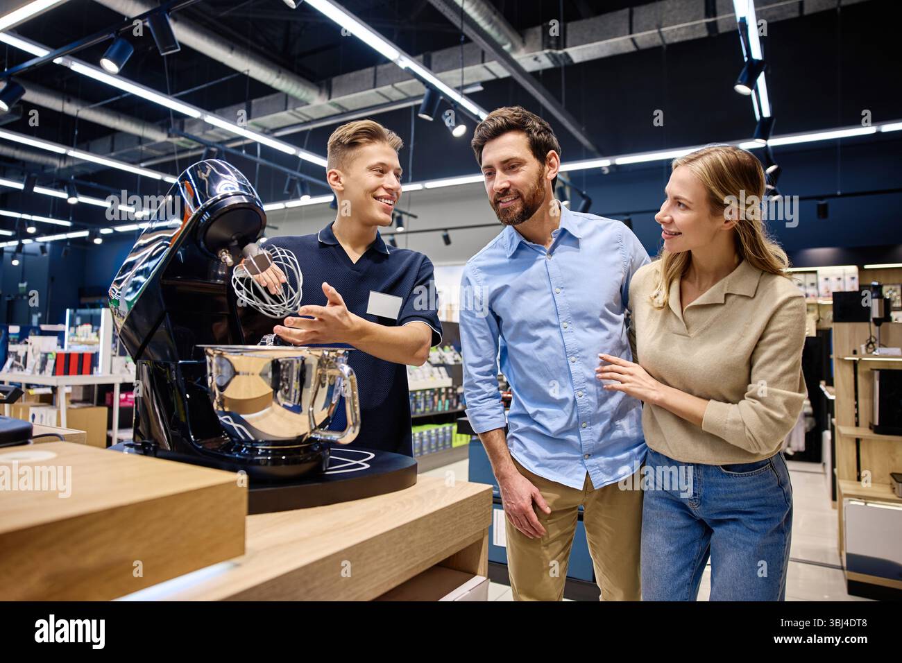 In einem geschäftigen Einzelhandelsgeschäft stellt ein sachkundiger Verkäufer einem interessierten Paar ein Hightech-Küchengerät vor, das seine einzigartige Leistung unterstreicht Stockfoto