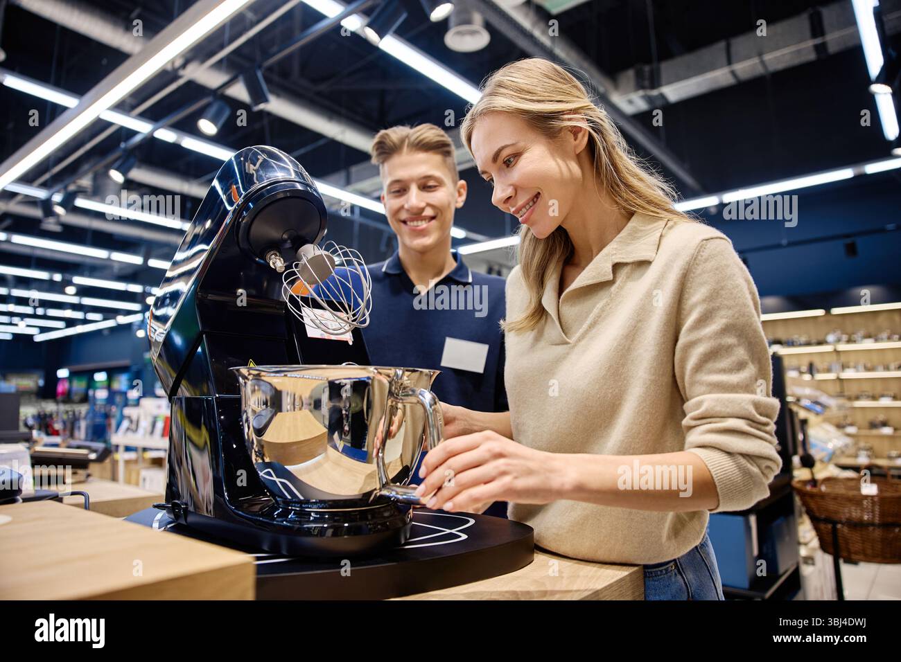 In einem geschäftigen Einzelhandelsgeschäft stellt ein sachkundiger Verkäufer einer interessierten Frau ein Hightech-Küchengerät vor und hebt dessen einzigartige Funktion hervor Stockfoto