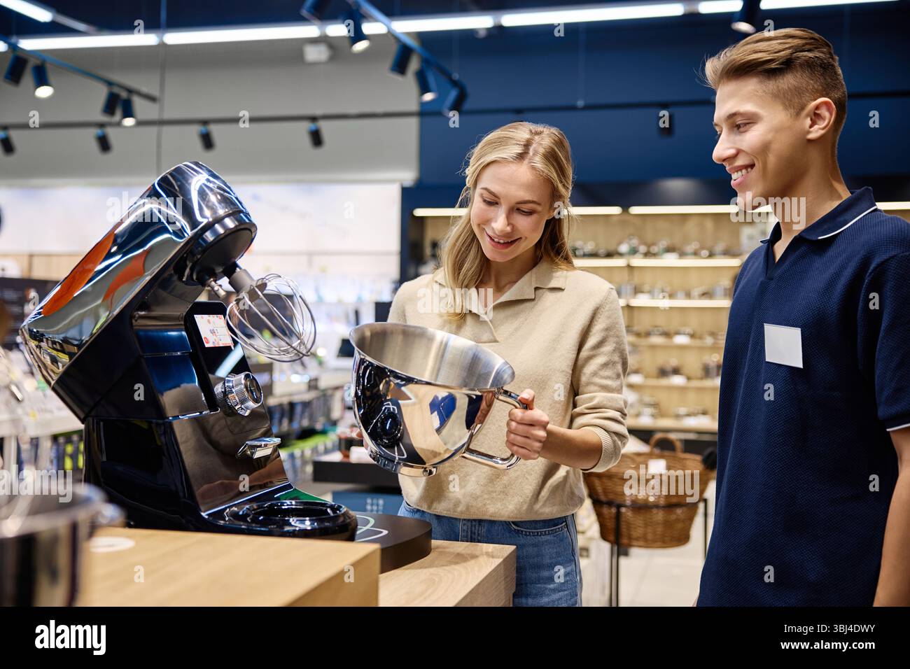 In einem geschäftigen Einzelhandelsgeschäft stellt ein sachkundiger Verkäufer einer interessierten Frau ein Hightech-Küchengerät vor und hebt dessen einzigartige Funktion hervor Stockfoto