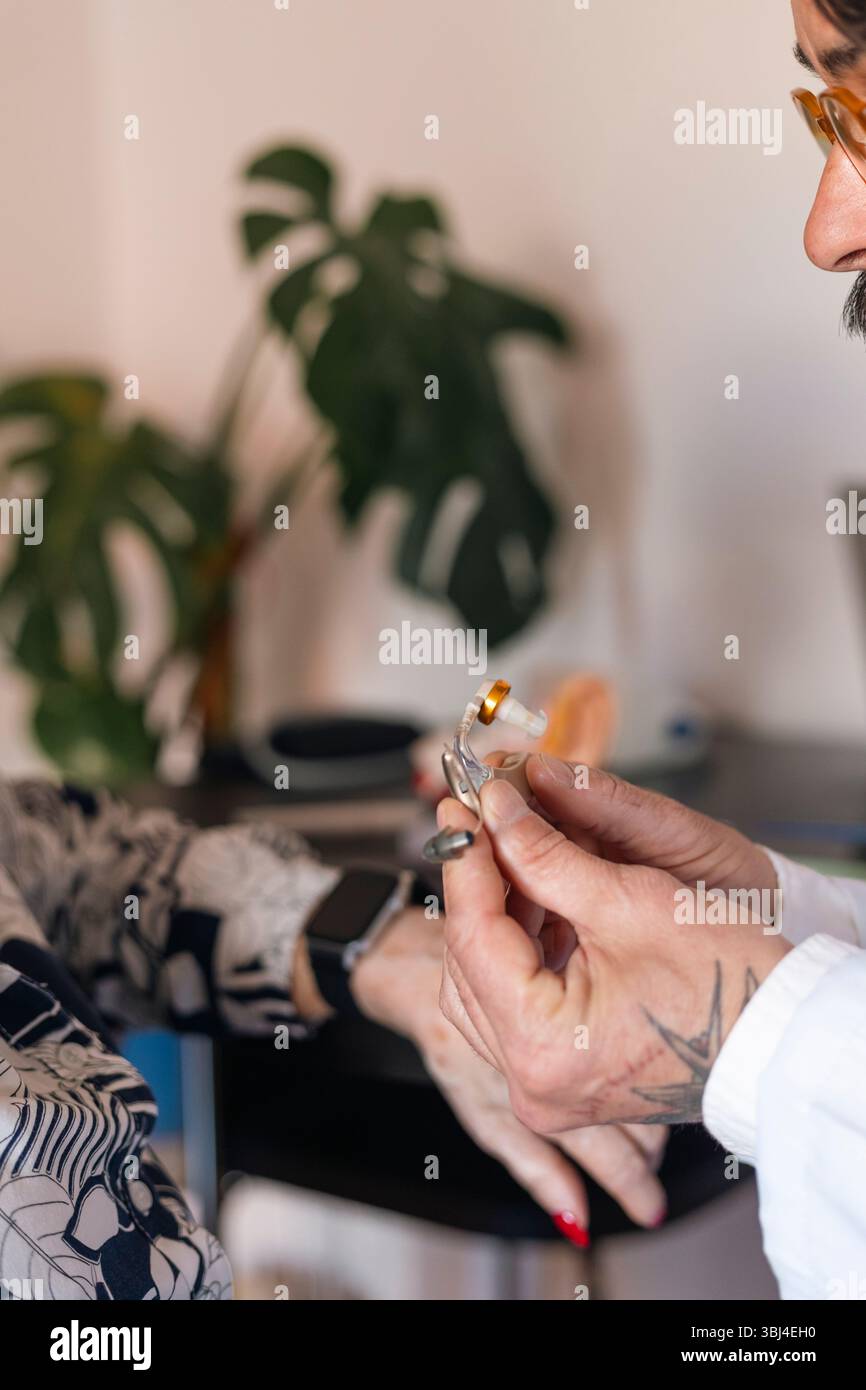 Tätowierte Hände bei der Untersuchung eines kleinen Hörgerätes Stockfoto
