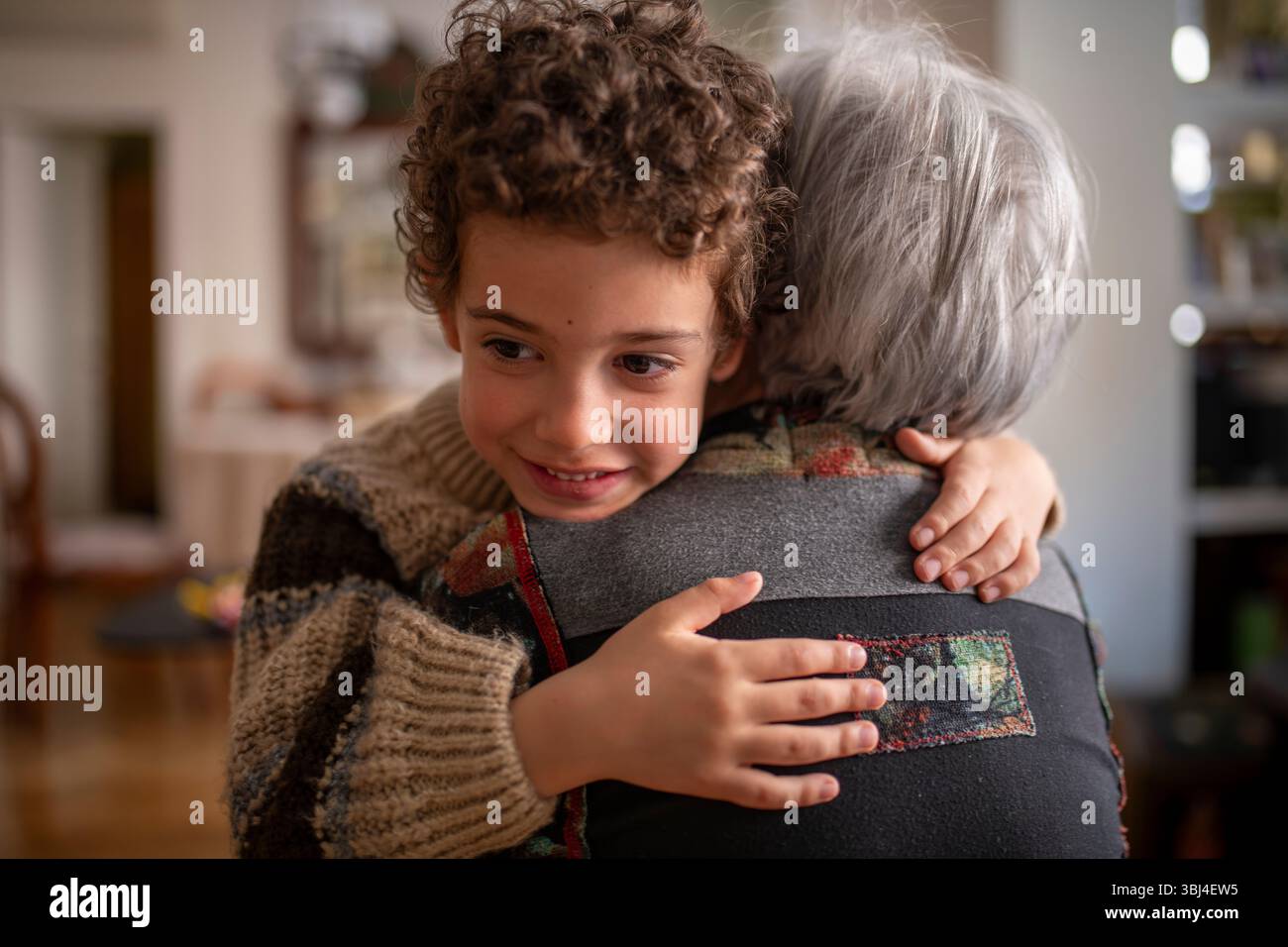 Glückliches Enkelkind, das Großmutter zu Hause zärtlich umschließt und einen Moment der Zuneigung und Liebe genießt Stockfoto