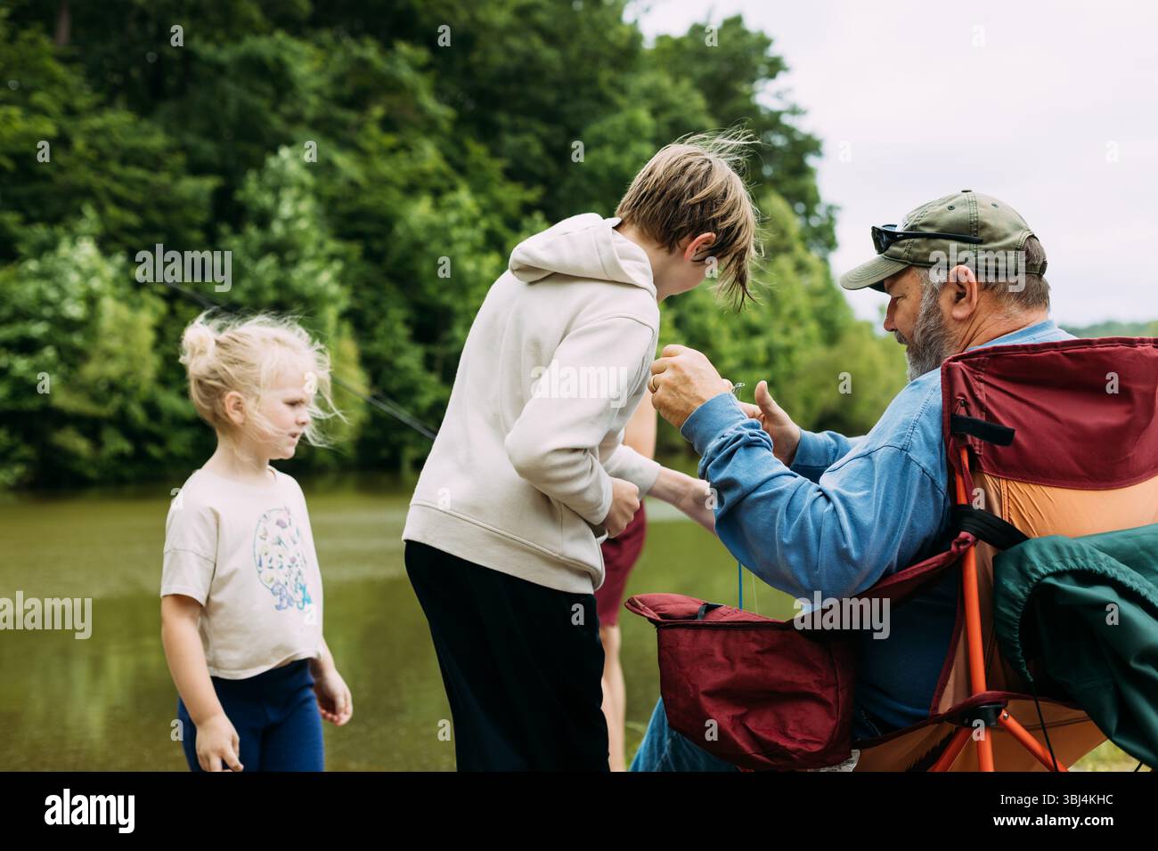 Opa hilft Enkelkindern beim Angeln am Memorial Day-Wochenende am See Stockfoto
