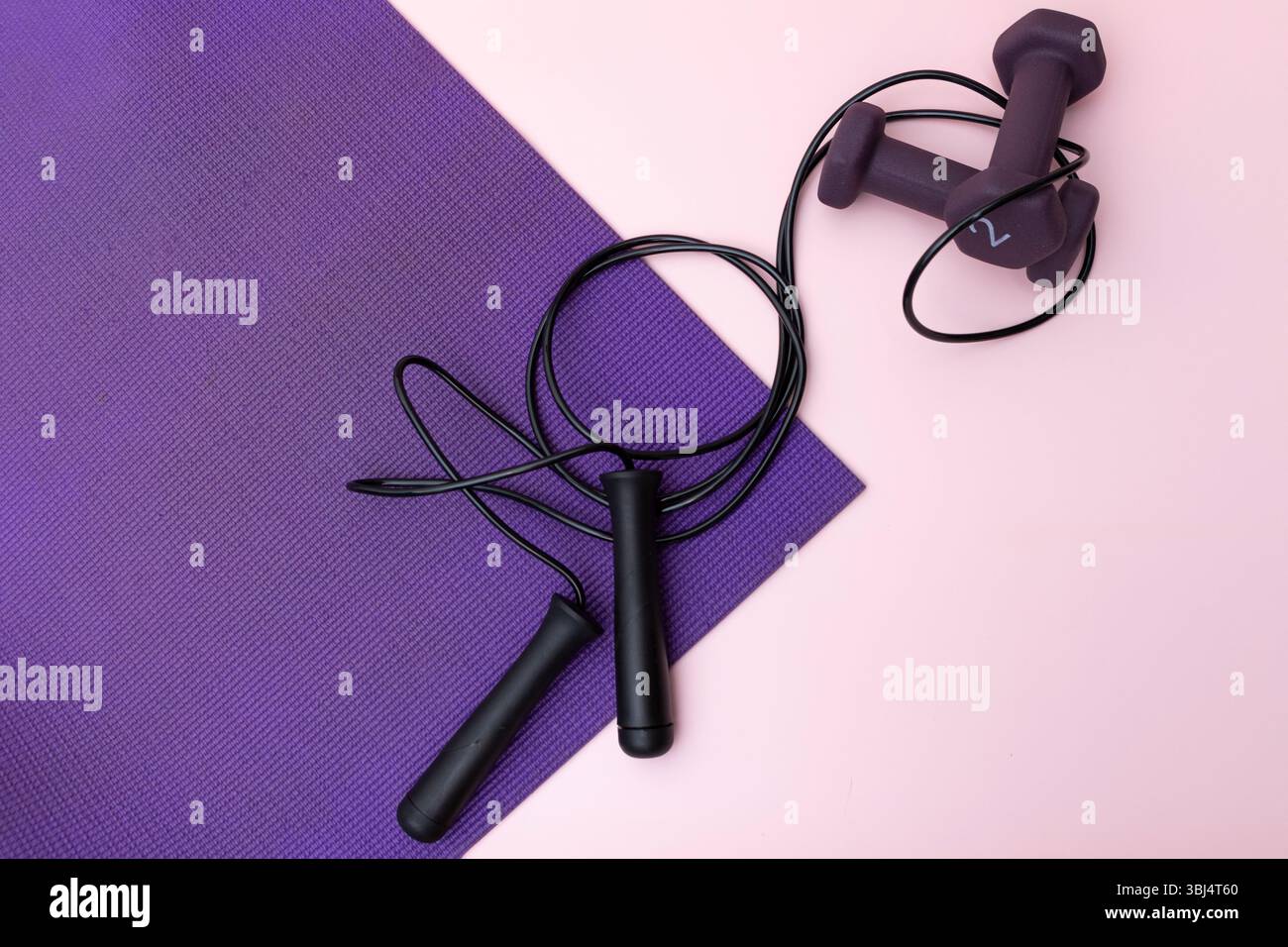 Springe mit Seil und Kurzhanteln auf lila Yogamatte mit rosa Hintergrund Stockfoto