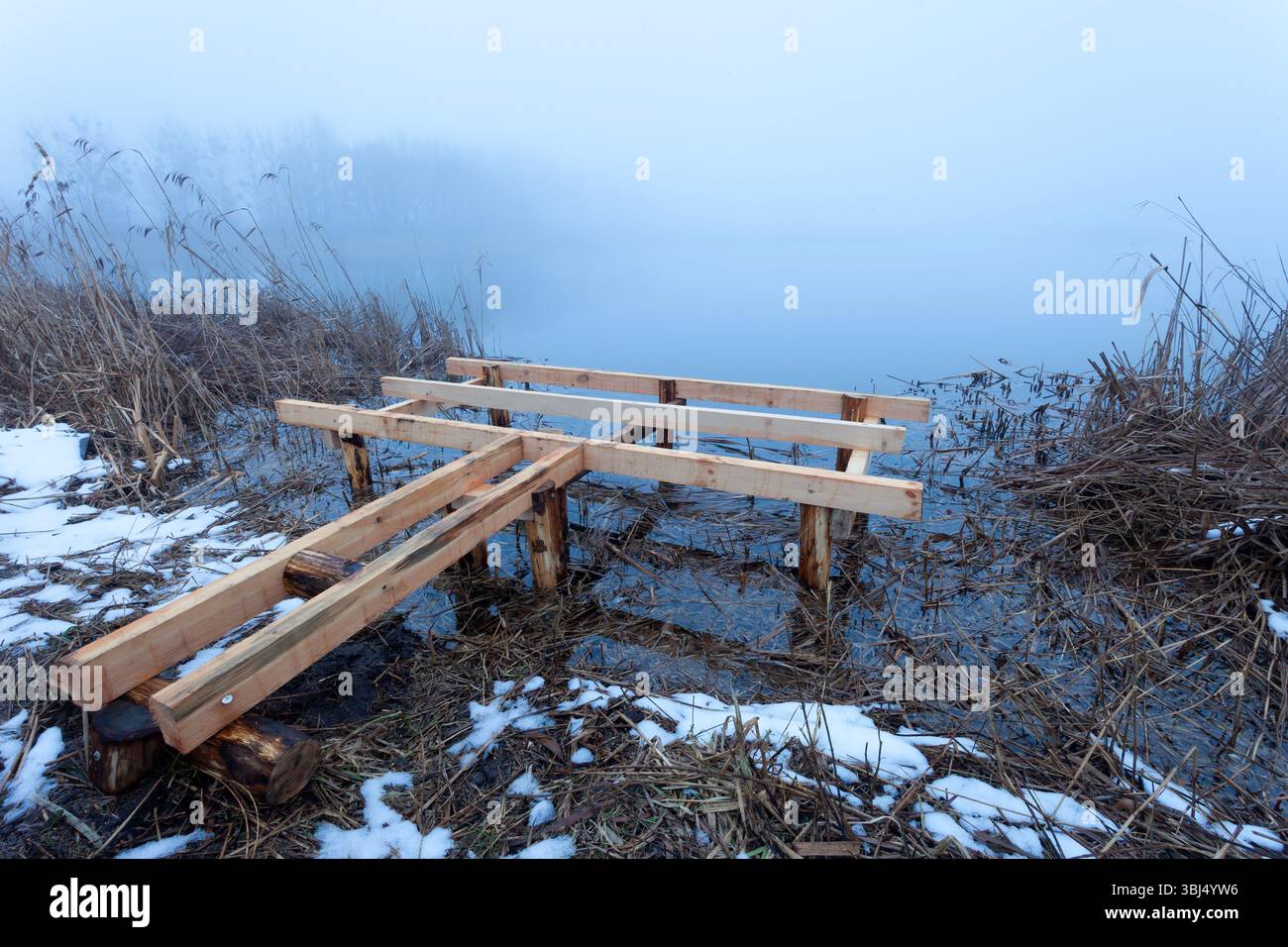 Bau eines neuen Holzsteges am Ufer eines nebeligen Sees Stockfoto