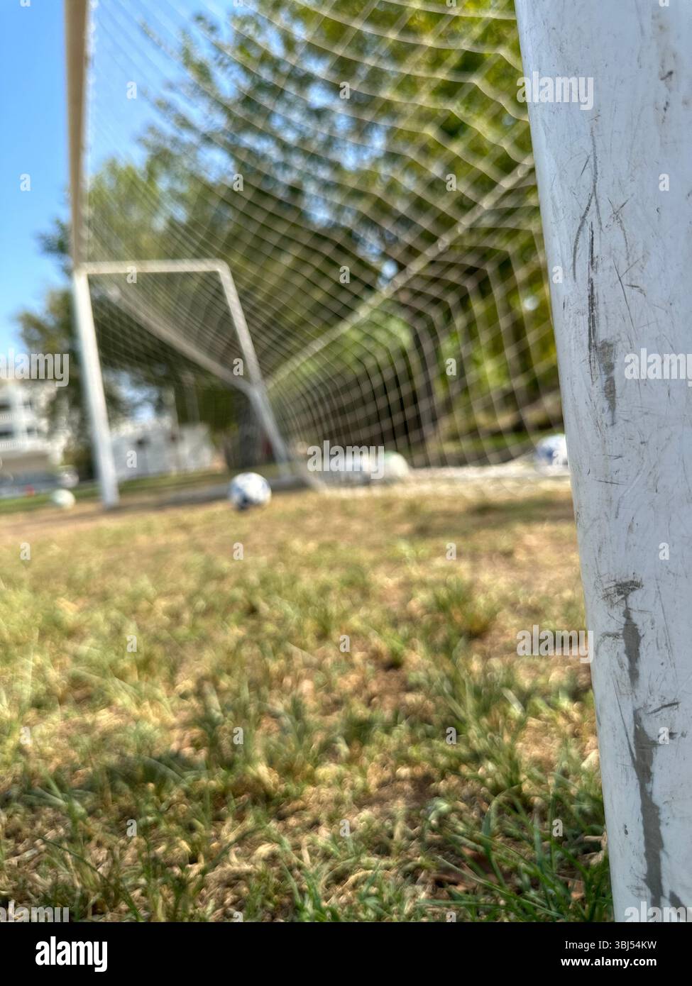 Fußball auf grünem Gras in der Nähe des Tornetzes unter sonnigem Himmel, Nahaufnahme des Fußballfeldes Stockfoto