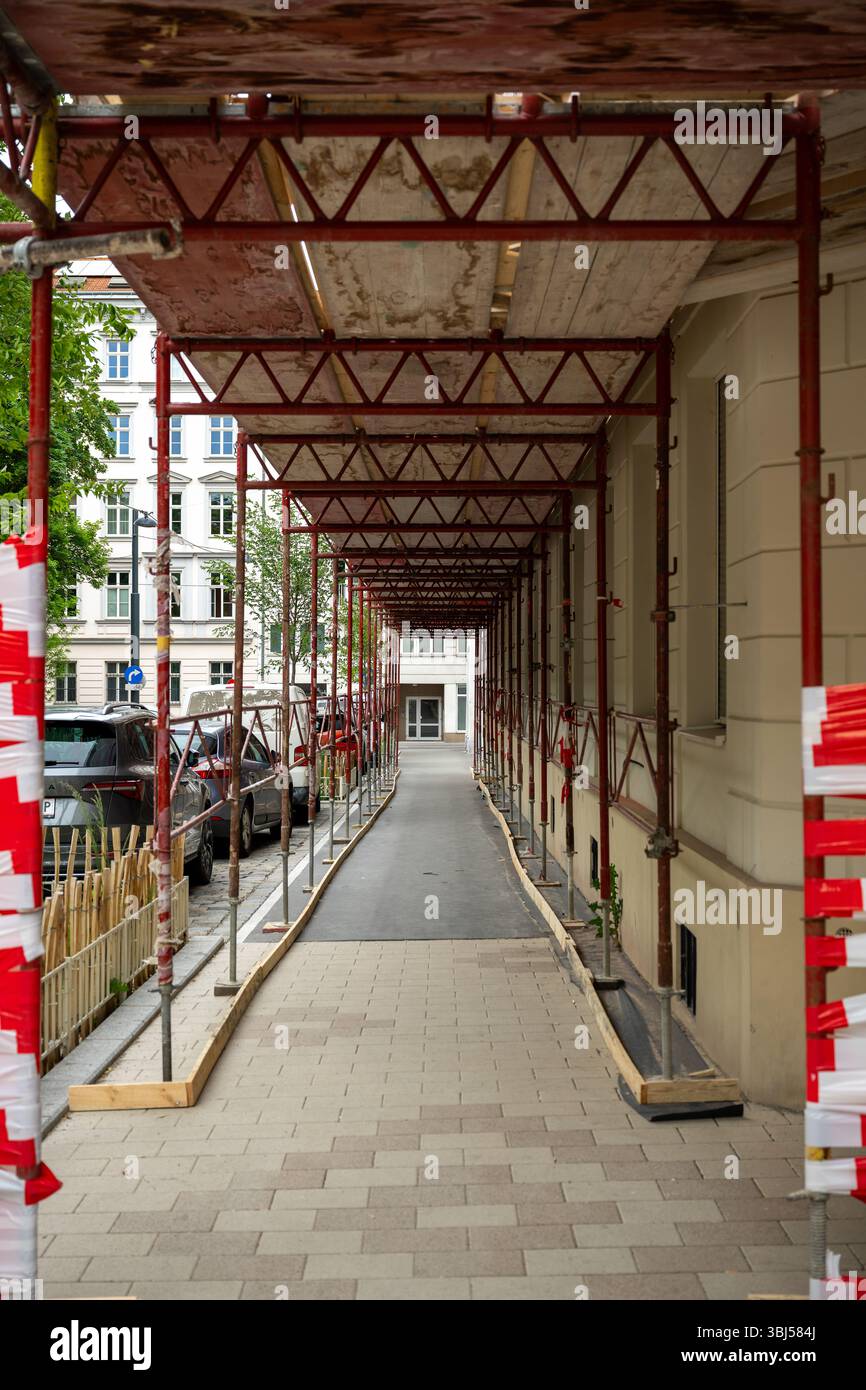 Überdachter Fußgängerweg unter rotem Gerüst neben dem Gebäude, Konzept des Stadtbaus Stockfoto