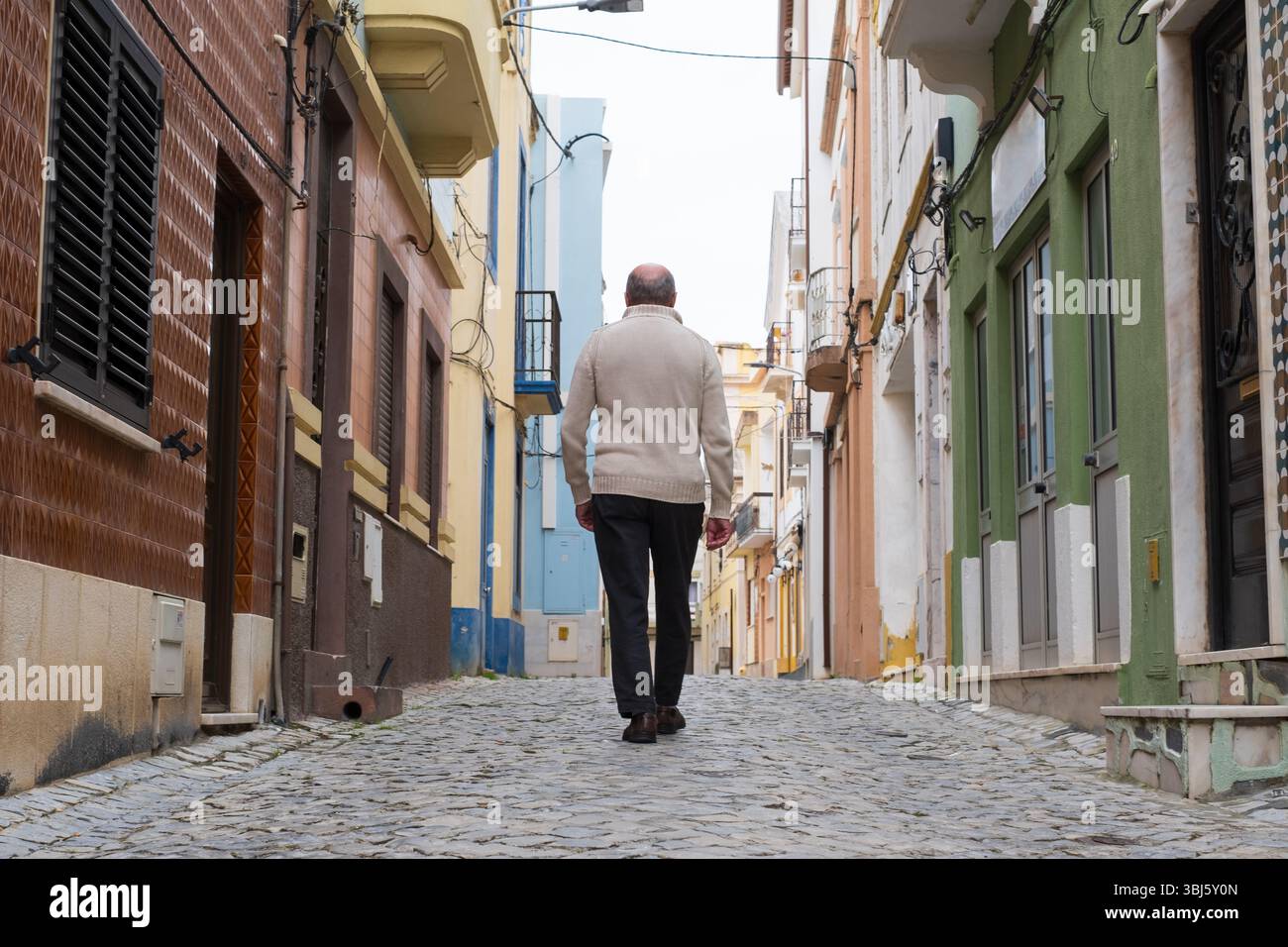 Ein älterer Mann, der eine enge portugiesische Straße hinunterläuft, von hinten gesehen. Stockfoto