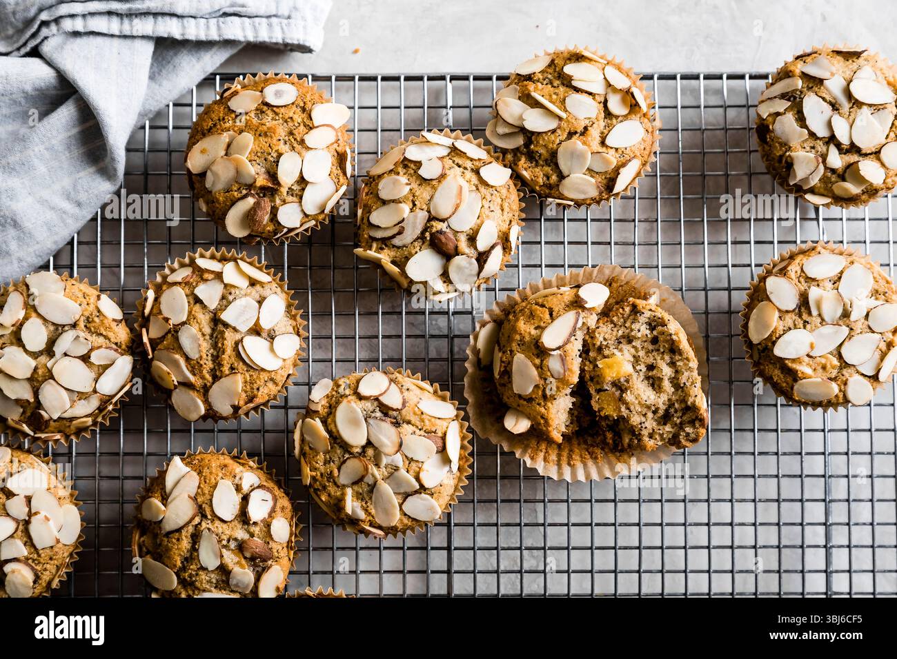 Muffins mit Mandelstopfen, die auf einem Gittergestell mit einer Stoffserviette in der Nähe abkühlen. Stockfoto