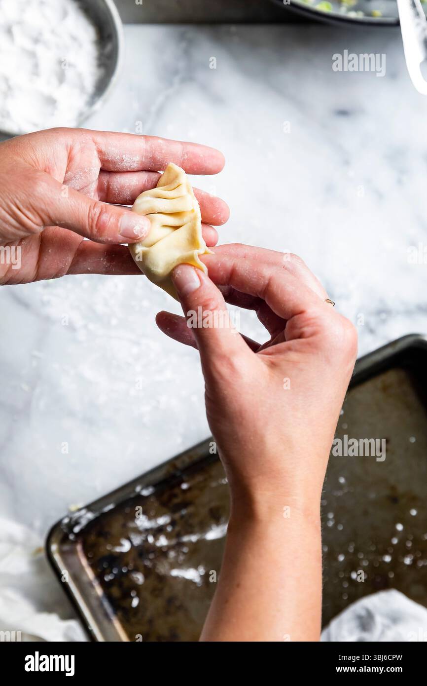 Eine Person faltet einen Knödel auf einer bemehlten Oberfläche. Stockfoto