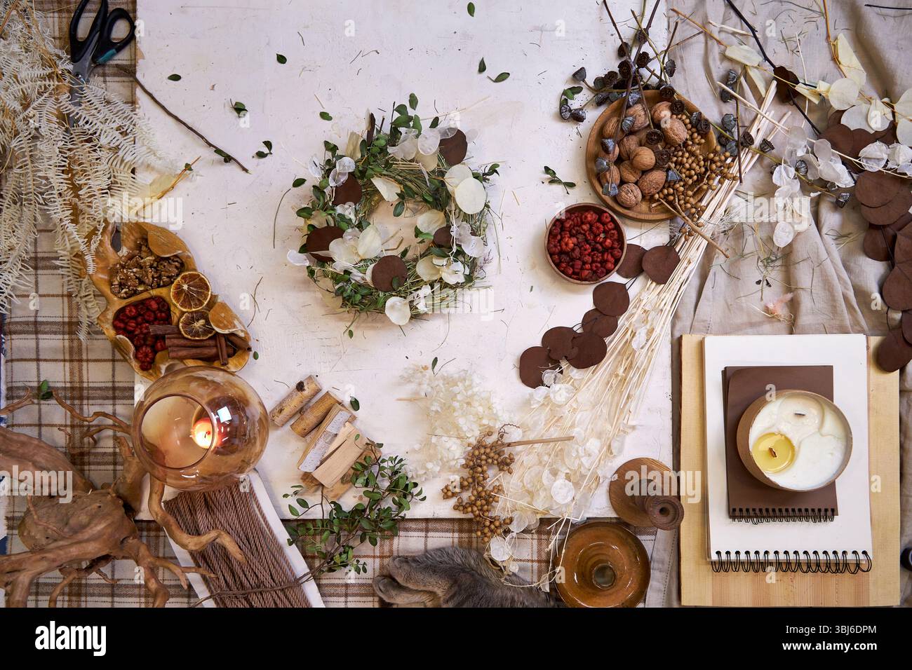Flaches Legen eines fertigen handgefertigten getrockneten Blumenkranzes auf einem hellen Holztisch, umgeben von Bastelmaterialien wie getrockneten Blumen, Garn Stockfoto