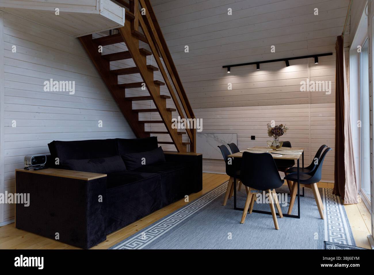 Dieses Bild zeigt einen modernen Wohnbereich mit einem eleganten schwarzen Sofa, geschmackvollem Dekor und einem Esstisch in einem harmonischen Design, das an conte erinnert Stockfoto