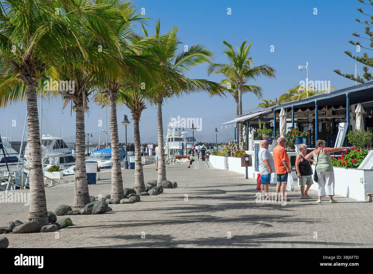 Puerto Calero mit Palmen und Yachthafen, touristische Gruppe von Freunden, die sich das Menü vor dem Restaurant Lanzarote im Freien ansehen Stockfoto