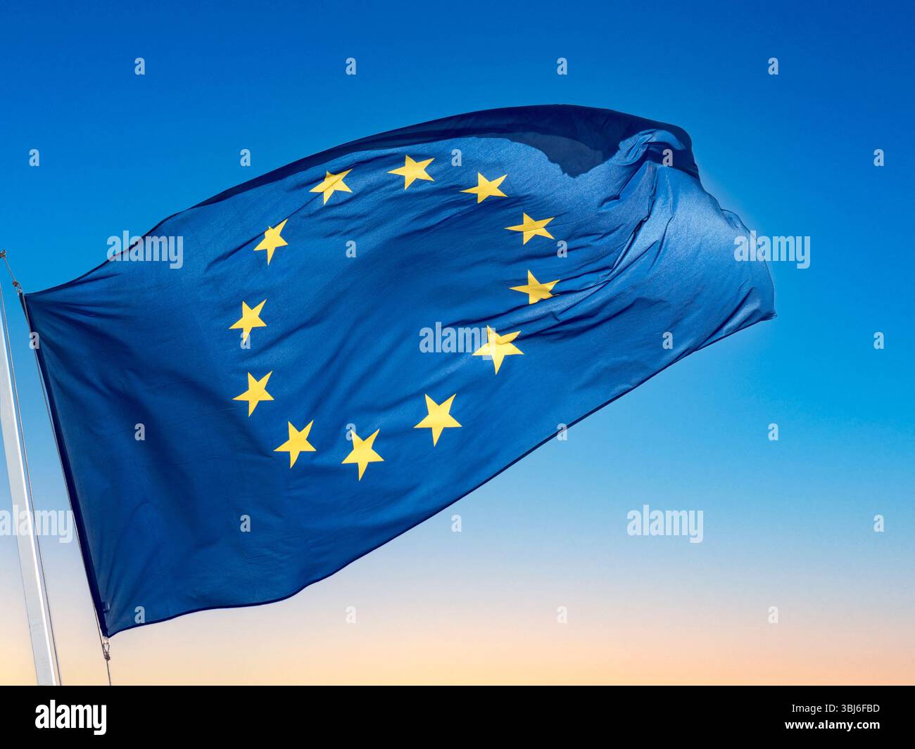 EU-FLAGGE fliegender Sonnenuntergangshimmel sonnig Smart bold EU EU-Flagge fliegt flatternd Frostaktion im Wind hinterleuchtet vor blauem, klarem Himmel Stockfoto
