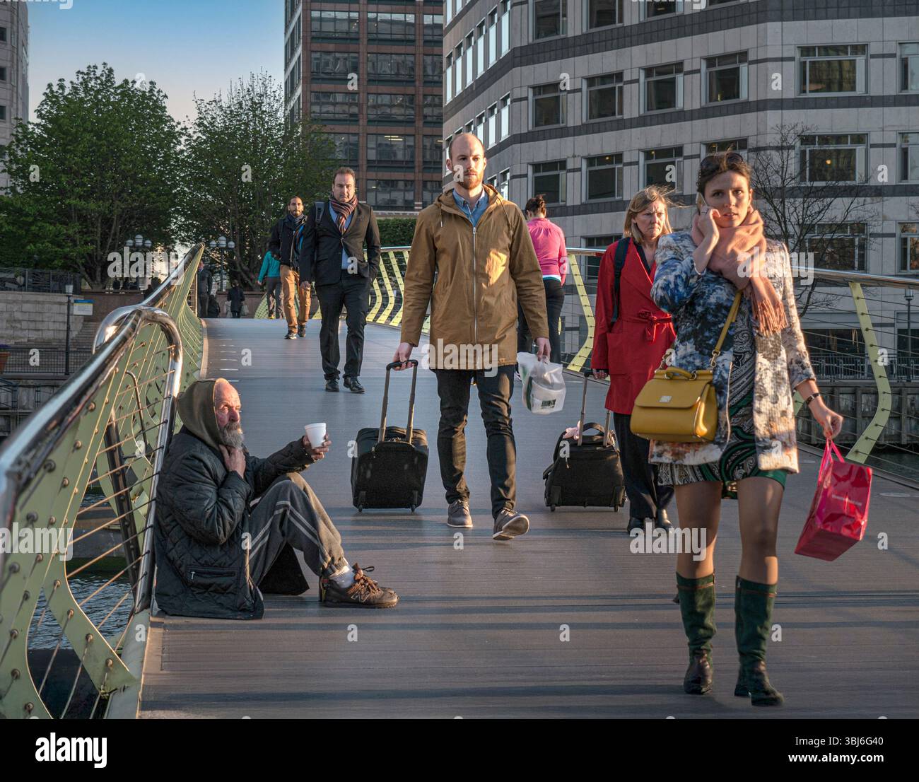 STADTARBEITER BETTELN CUP BETTLER STADT Canary Wharf Londoner Arbeiter sind klug gekleidet in öffentlichen Finanzämtern, gehen an sitzenden älteren Mann vorbei, beleuchtet von der untergehenden Sonne, und fordern Bargeld mit seinem erweiterten Plastikbecher LONDON UK Stockfoto