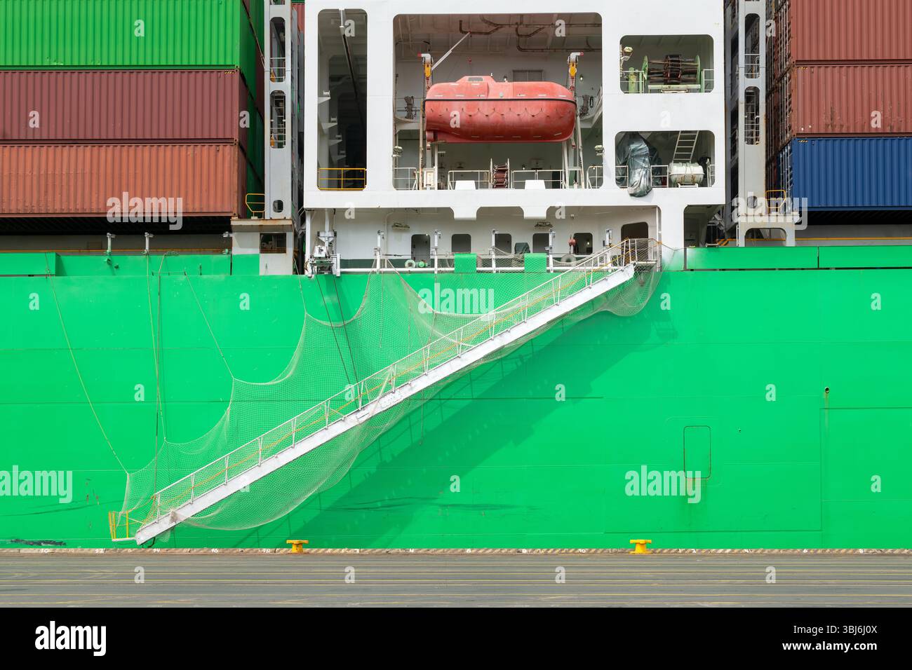 Ein belebtes, grünes Frachtschiff legte an und zeigte seinen Zugangsgang, ein Sicherheitsnetz und ein rotes Rettungsfloß. Einzelheiten zur maritimen Logistik. Stockfoto