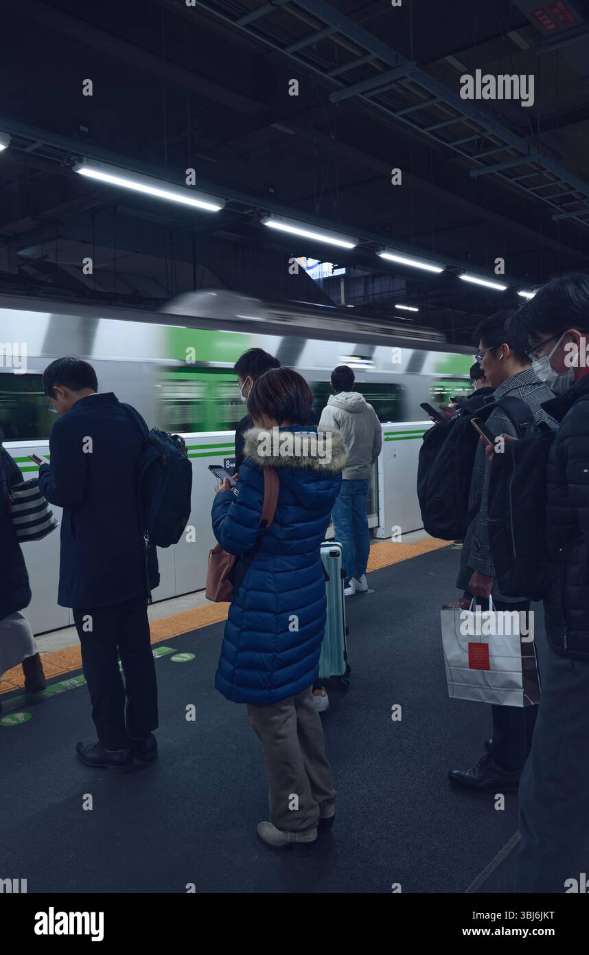 Lautlos wartend auf die Yamanote Line, beugten sich die Köpfe über ihre Telefone, während der Zug in einer unscharfen Bewegung vorbeigleitet Stockfoto