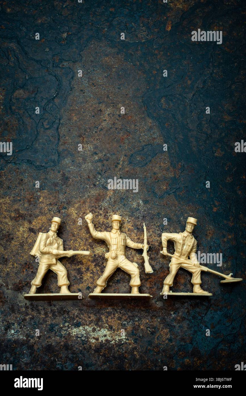 Drei Vintage-Spielzeugsoldaten in verschiedenen Stellungen ruhen auf einer robusten, strukturierten Oberfläche. Ihr spielerisches Erscheinungsbild weckt Erinnerungen an Kindheitskämpfe Stockfoto