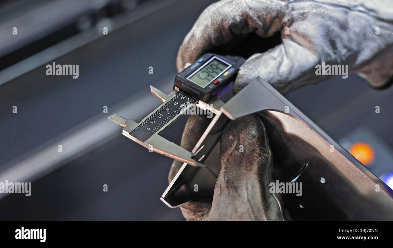 Arbeiter messen Metallteile mit digitalem Messschieber. Eine Hand mit Handschuhen verwendet einen digitalen Messschieber, um die Breite eines metallischen Bauteils genau zu messen. Stockfoto