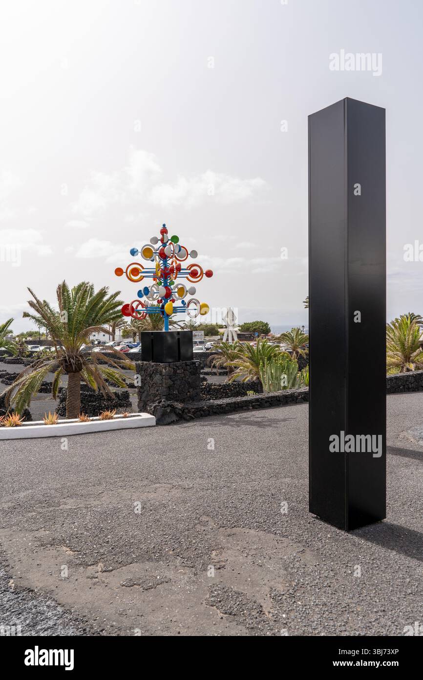 Neben einem schwarzen Obelisken steht eine farbenfrohe Skulptur. Diese Kunstszene spielt auf Lanzarote, Spanien. Stockfoto