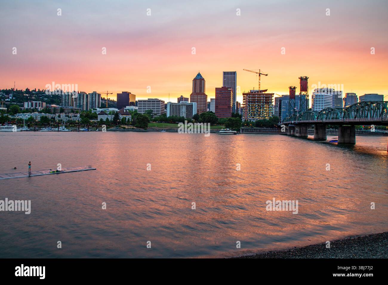 Portland, Oregon - 10. August 2018: Eine Person steht an einem Dock im Willamette River und genießt den Sonnenuntergang mit der Skyline von Portland. Stockfoto