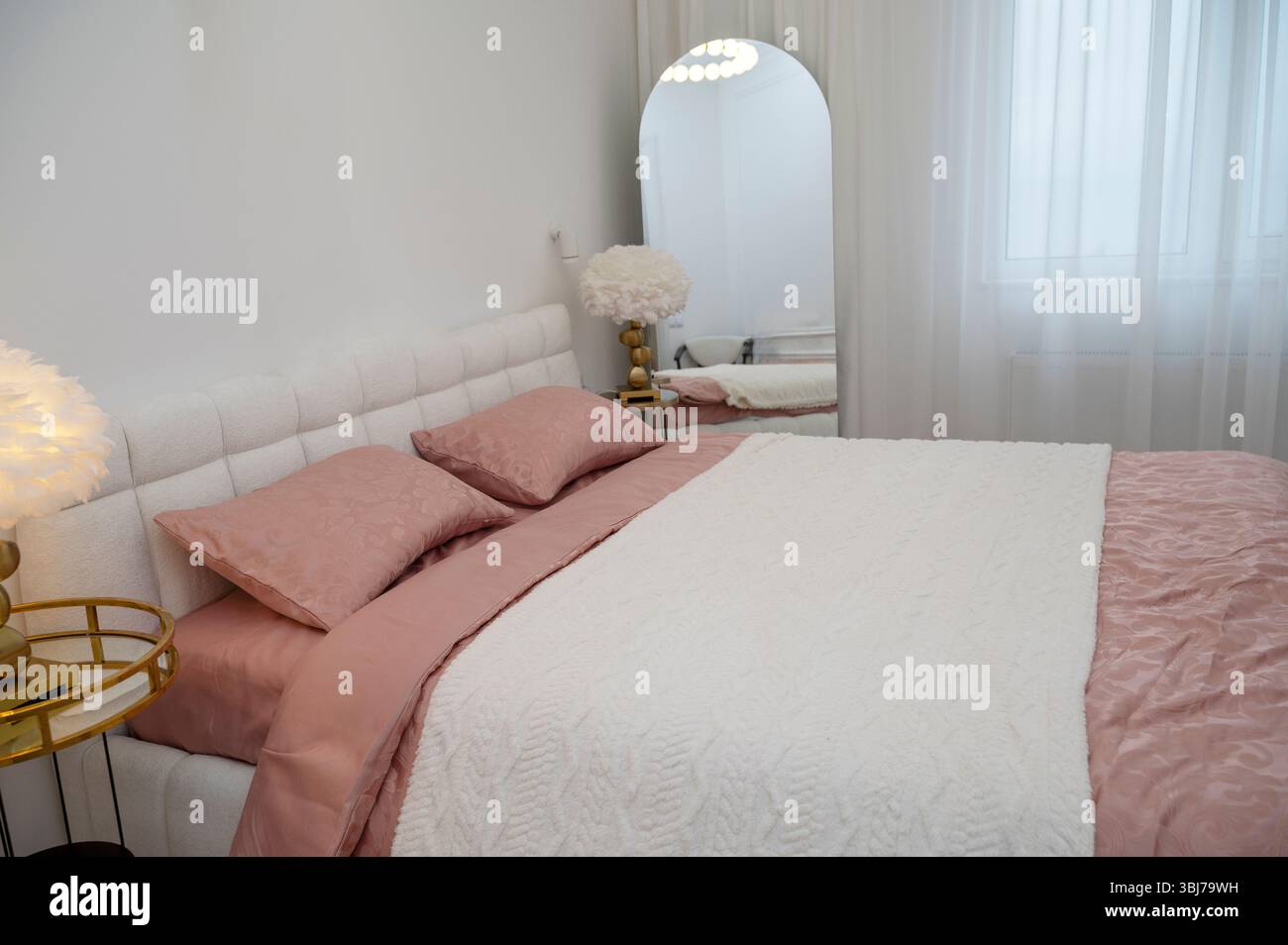 Doppelbett im Schlafzimmer mit dunkelrosa Bettwäsche und weißer Decke Stockfoto