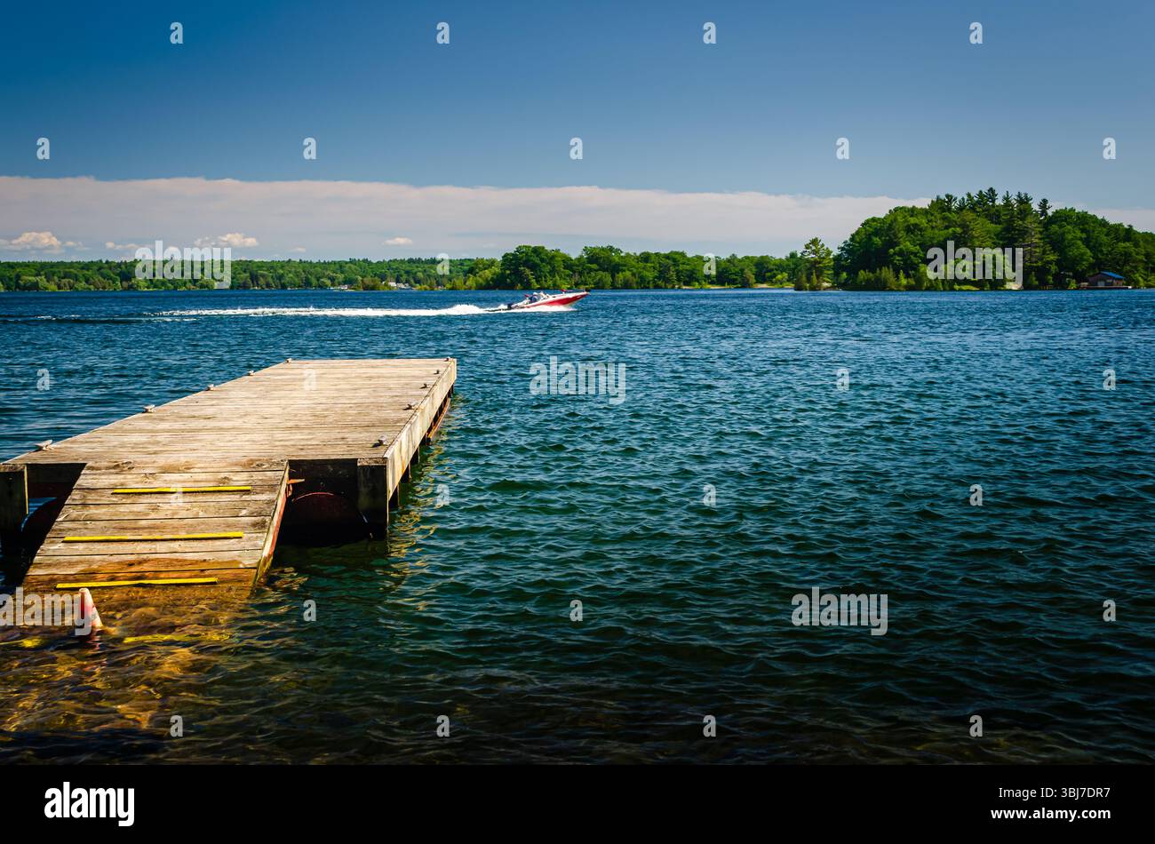 Untergetauchtes Dock mit einem vorbeifahrenden Schnellboot und Insel in der Ferne Stockfoto