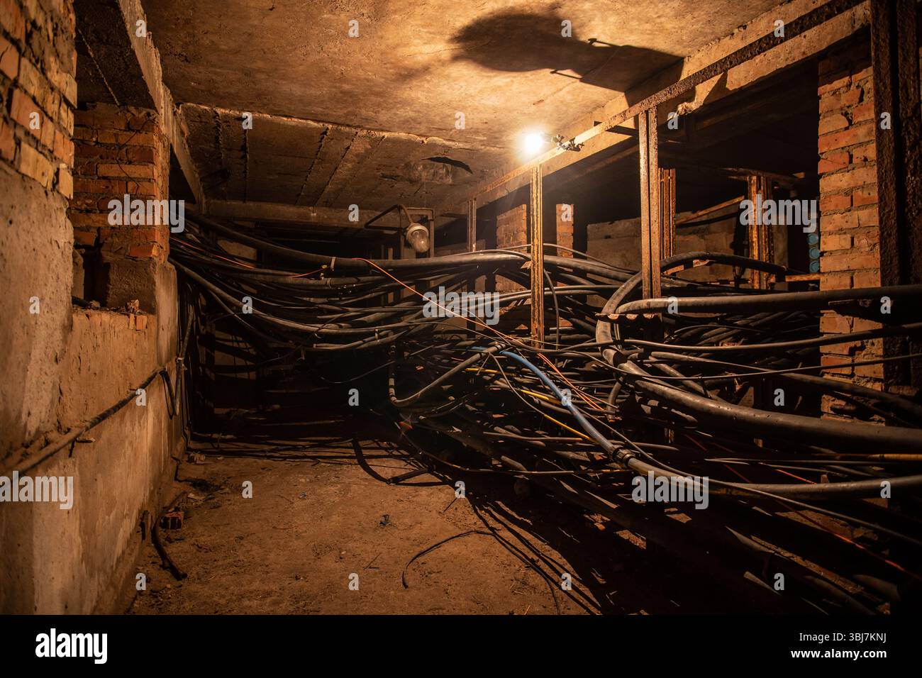 Ein alter unterirdischer Kabeltunnel oder Keller mit Kabeln mit Wolframlampen-Beleuchtung. Stockfoto