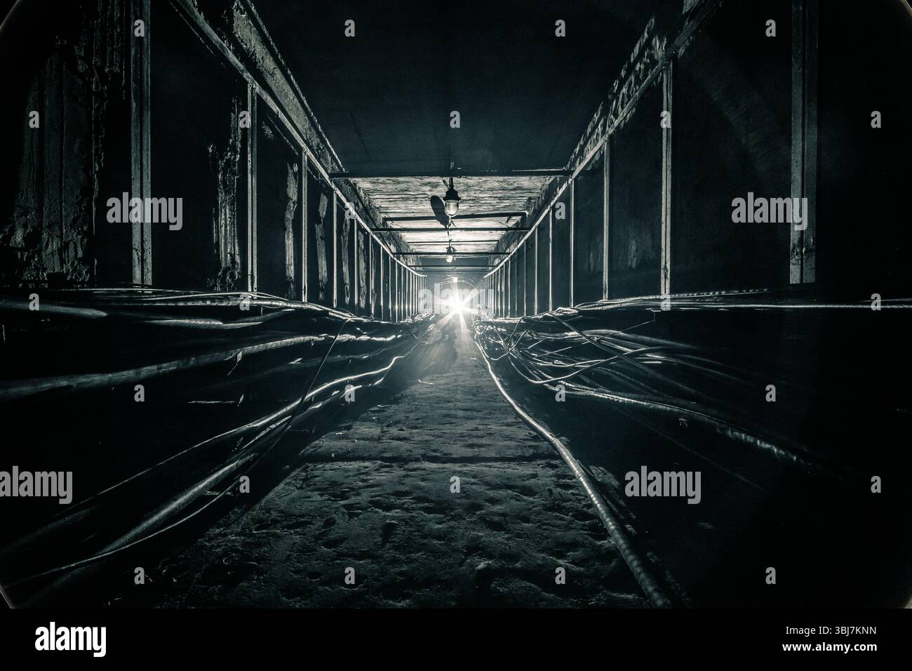 Der dunkle Betonkabeltunnel wird am Ende durch eine LED-Taschenlampe beleuchtet Stockfoto