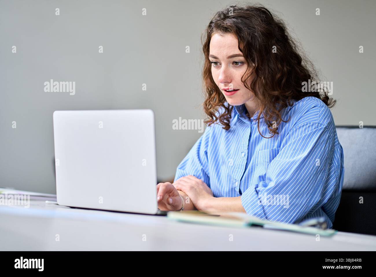Junge Geschäftsfrau, die am Schreibtisch sitzt und an einem Laptop arbeitet. Stockfoto
