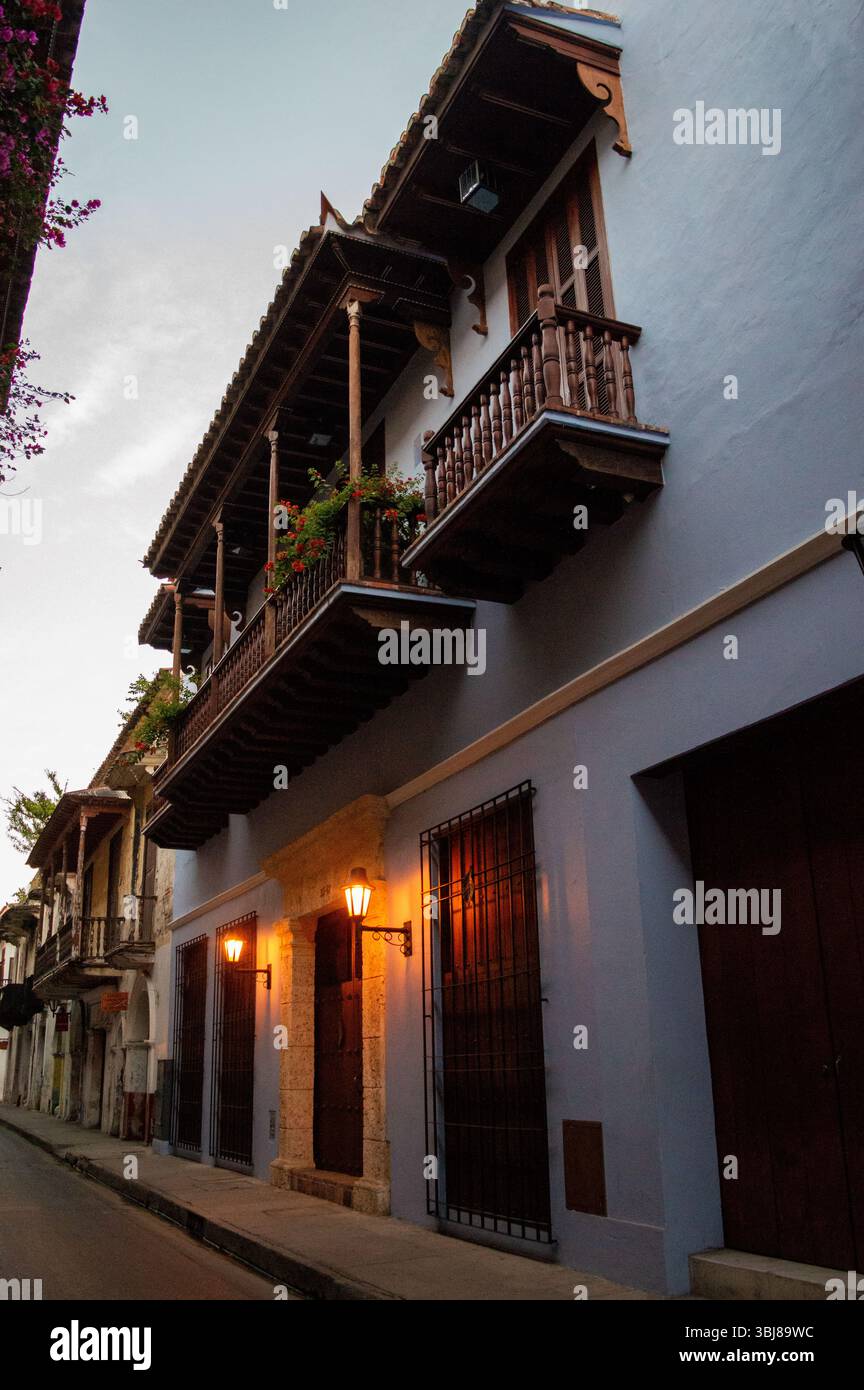Wunderschönes Kolonialgebäude mit Holzbalkonen und warmen Straßenlaternen, die Cartagenas lebhafte Atmosphäre während des Sonnenuntergangs zum Ausdruck bringen. Stockfoto