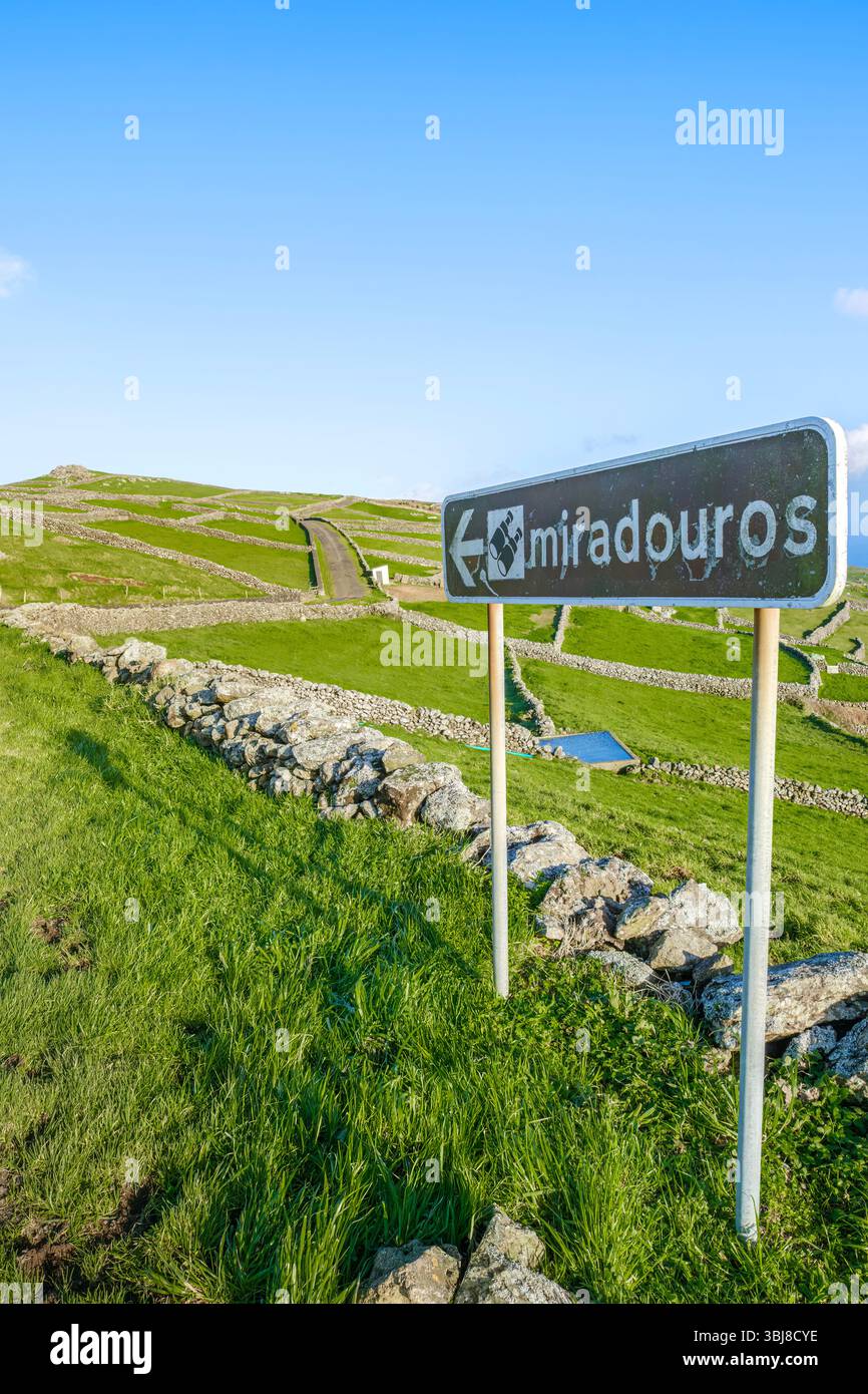 Ein rustikales „Miradouros“-Schild zeigt auf malerische Aussichtspunkte inmitten üppiger grüner Hügel, die von traditionellen Trockenmauern in der Azoren-Region segmentiert sind Stockfoto