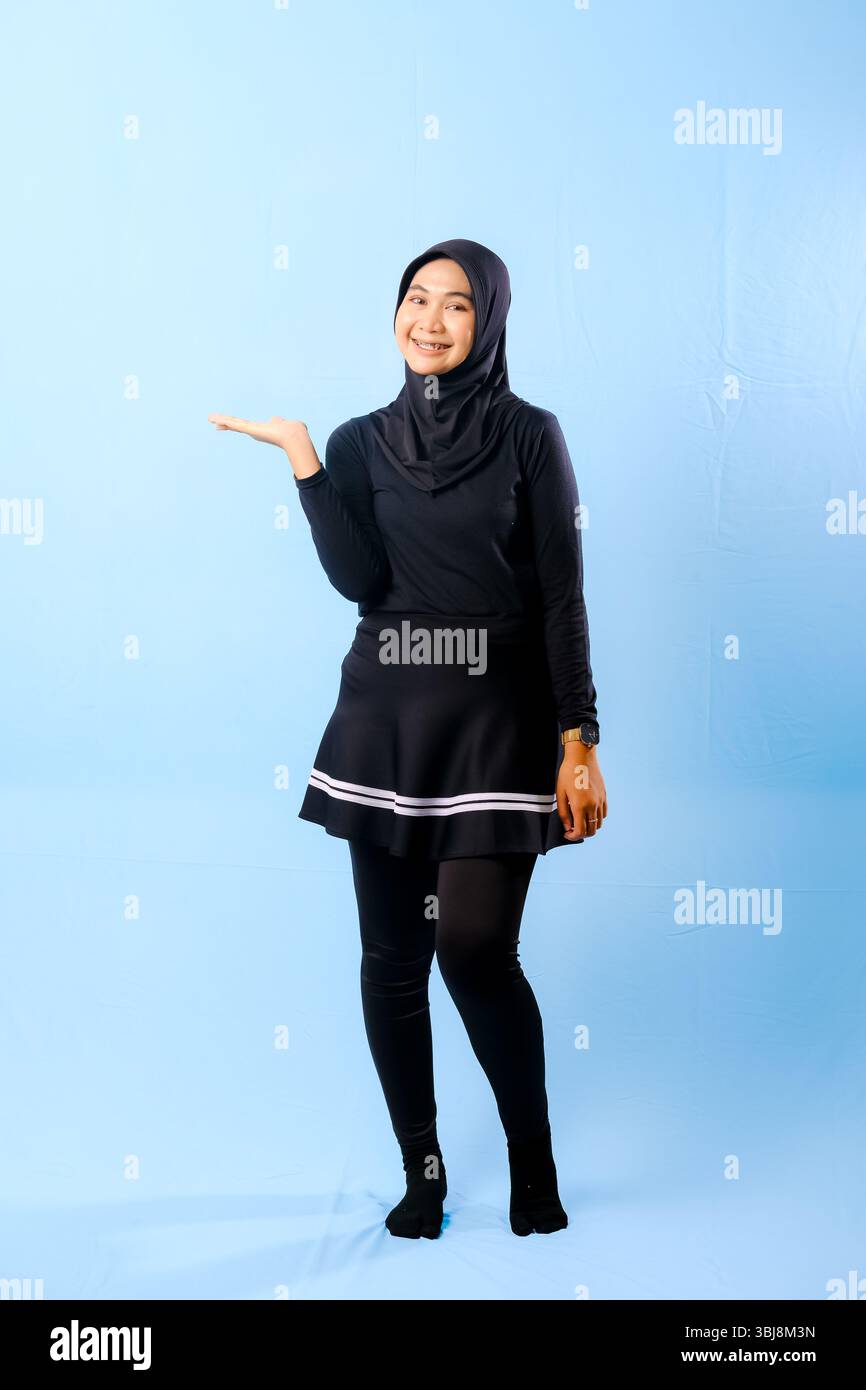 Eine Frau mit schwarzem Rock und schwarzer Hose. Sie lächelt und hält ihre Hand hoch Stockfoto