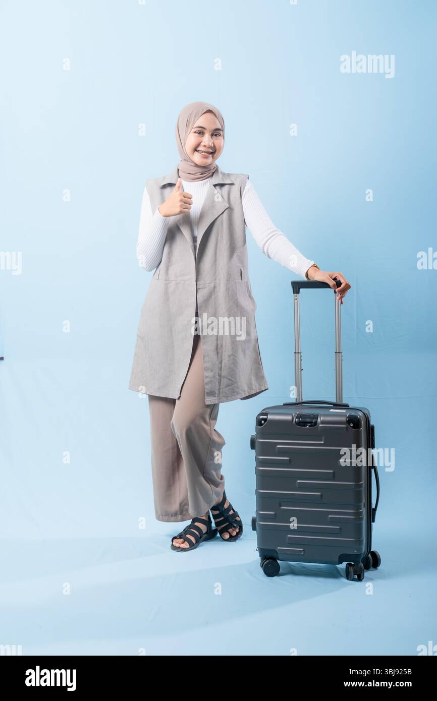Eine Frau posiert mit einem Koffer und gibt die Daumen hoch. Das Konzept der Spannung und des Abenteuers, während die Frau bereit ist, sich auf eine Reise zu begeben Stockfoto