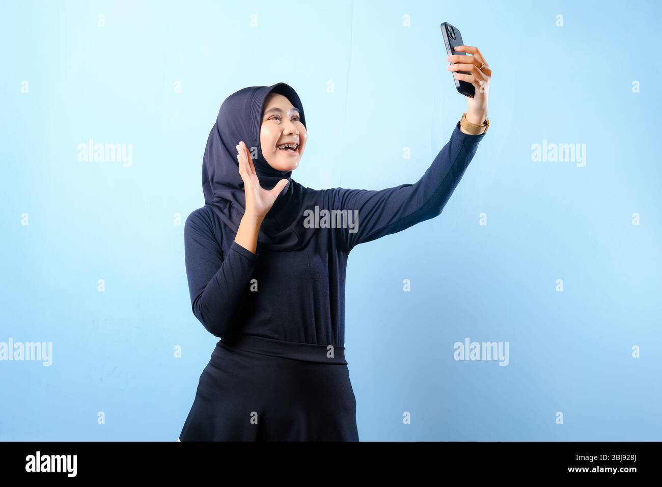 Eine Frau, die einen schwarzen Hijab trägt, macht ein Selfie mit ihrem Handy. Sie lächelt und ist glücklich Stockfoto