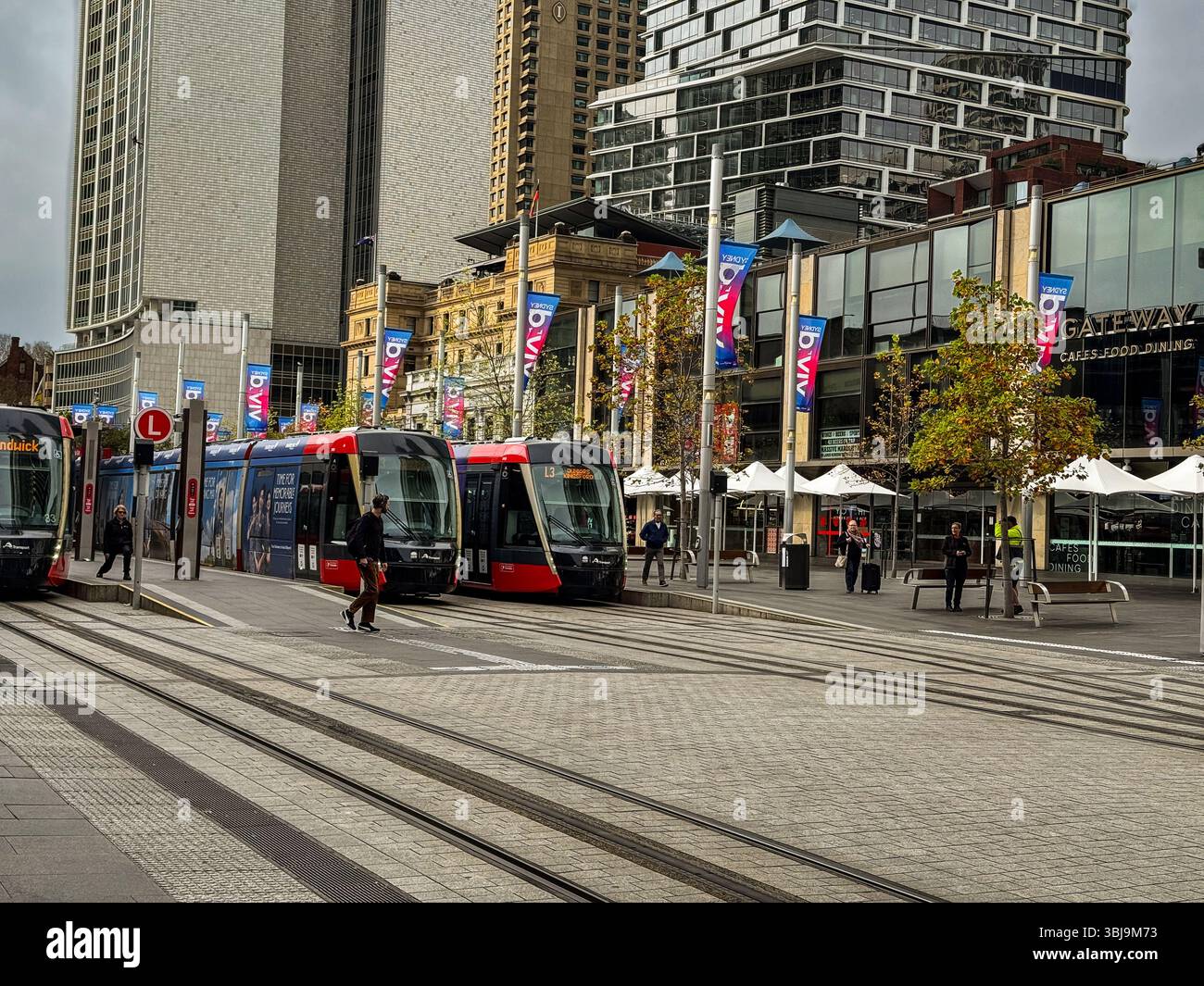 Moderne Straßenbahnen an der Circular Quay Station in Sydney, Australien, mit Stadtgebäuden, Fußgängern und Vivid Sydney Festivaldekorationen Stockfoto