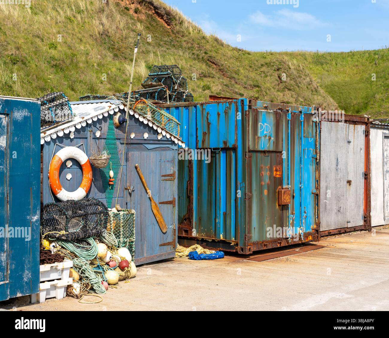 13. Juni 2025. Port Errol, Cruden Bay, Aberdeenshire, Schottland. Dies ist eine hölzerne Fishermans Hut zwischen Metallcontainern am Pier of the Harbor am Hafen Stockfoto