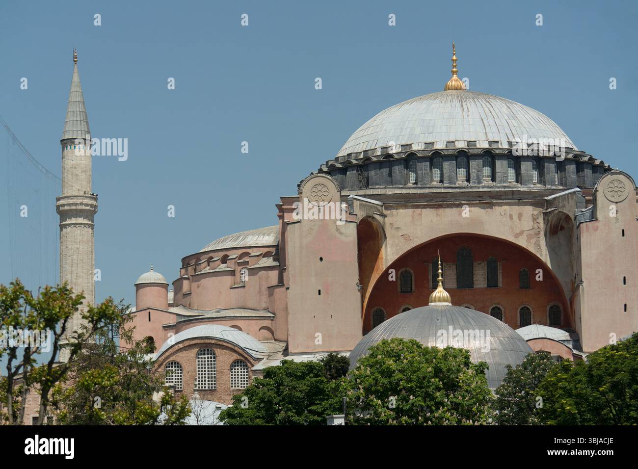 Besucher bewundern die beeindruckende Architektur der Hagia Sophia mit ihrer großen Kuppel und dem Minarett, umgeben von üppigem Grün in Istanbul. Stockfoto