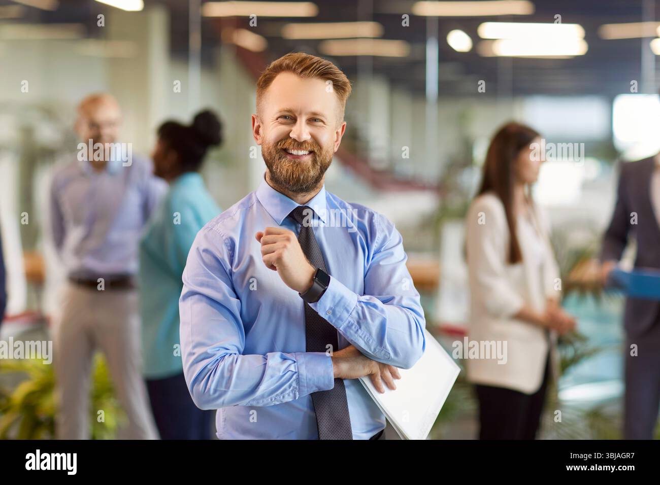 Glücklicher, bärtiger junger Geschäftsmann, der in die Kamera blickt und im Büro lächelt. Stockfoto