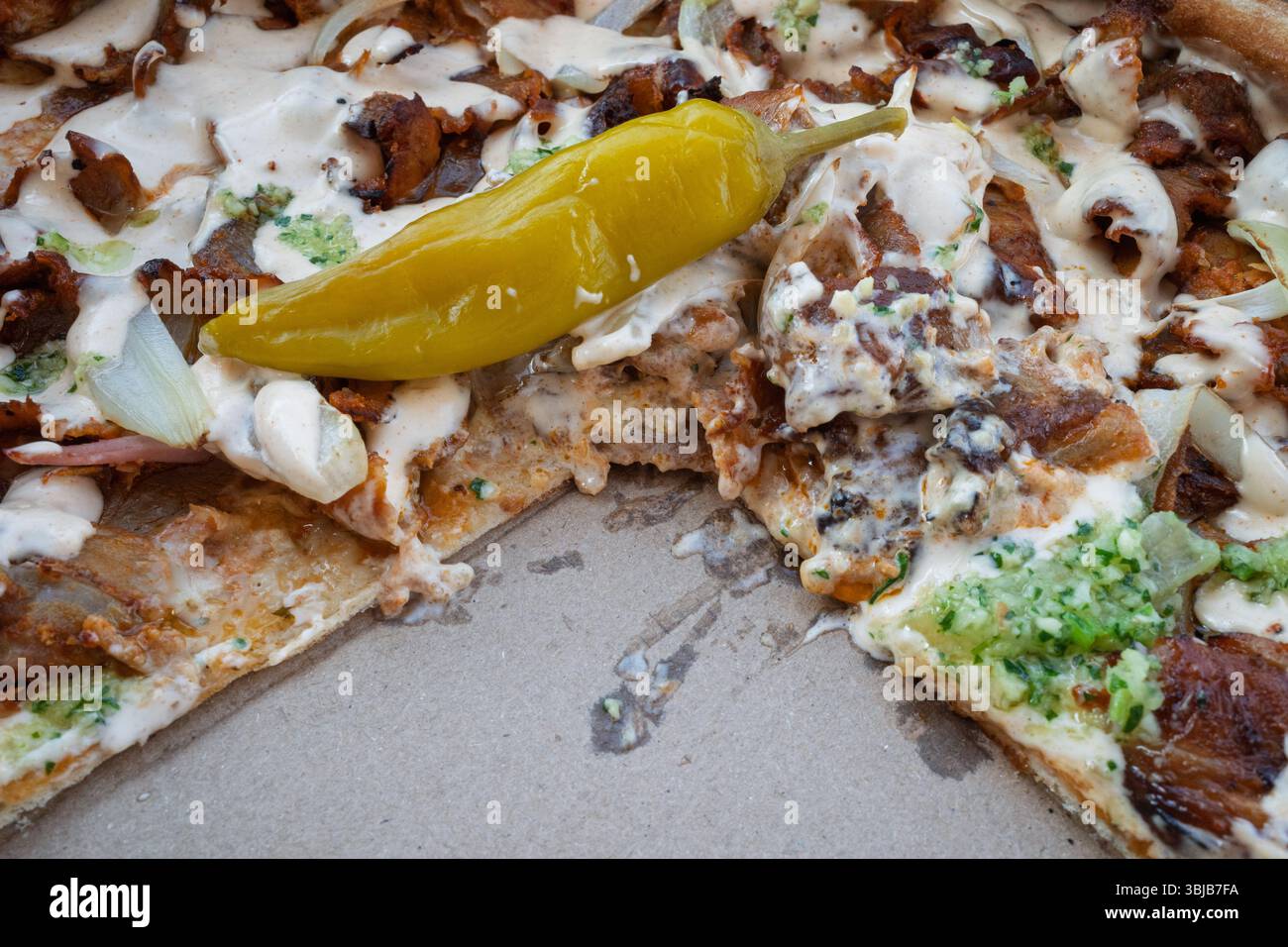 Eine halbgefressene Döner-Pizza in Nahaufnahme, cremiger Sauce, mit einem würzigen, eingelegten Pfeffer, immer noch verführerisch in der Kiste. Stockfoto