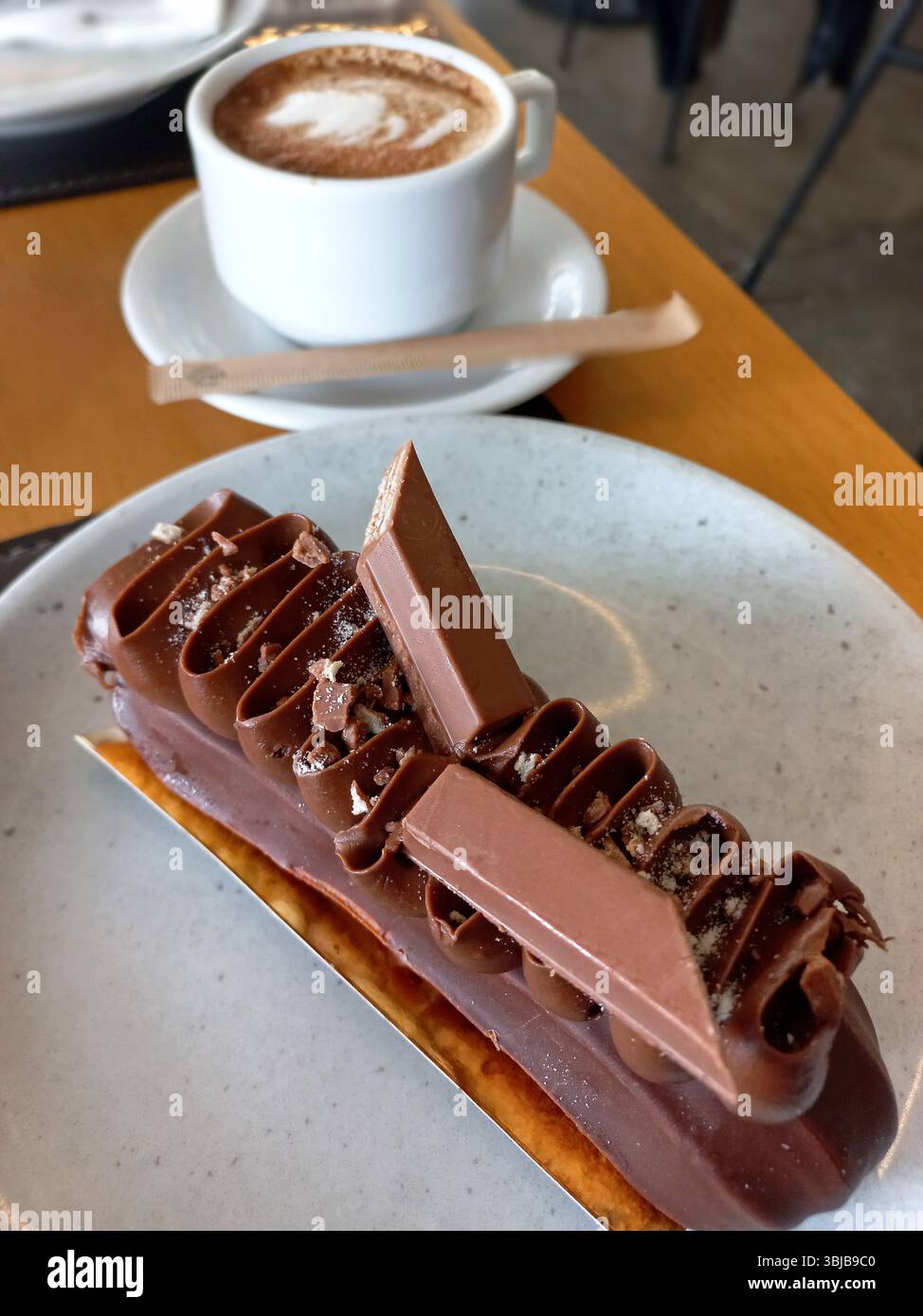 Elegantes Schokoladengebäck mit Mousseschichten und dekorativen Schokoladensplittern, serviert mit einer Tasse Kaffee auf einem Kaffeetisch Stockfoto