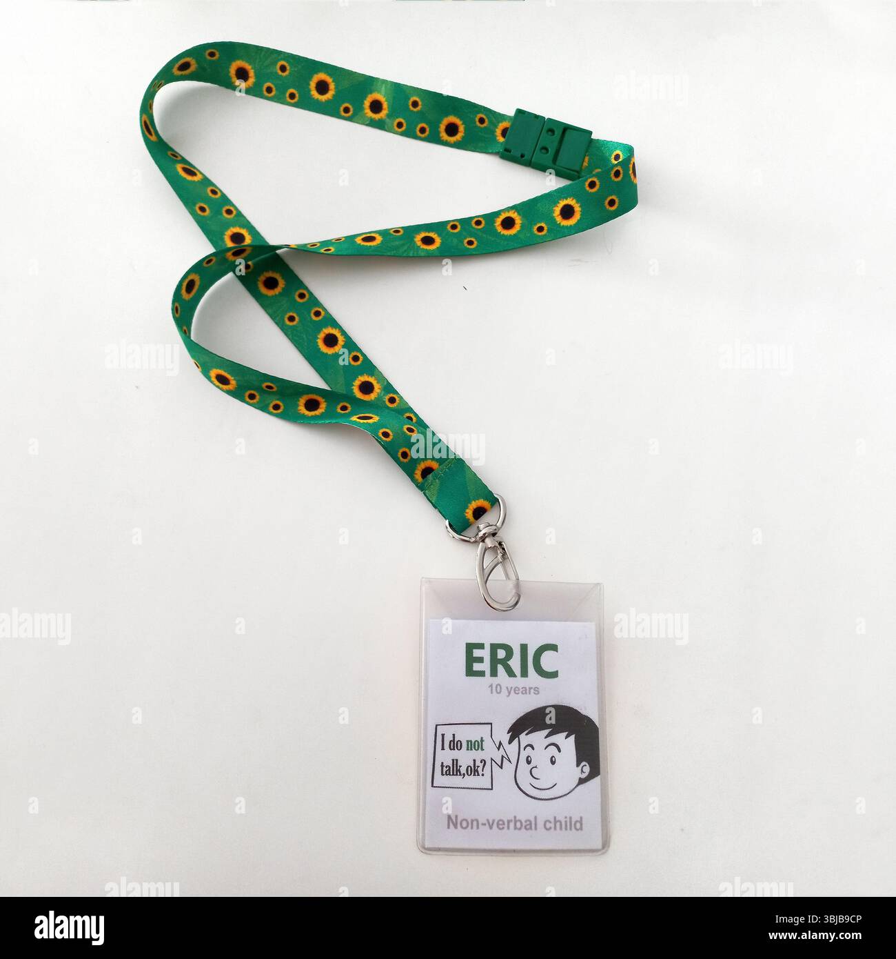 Grünes Lanyard mit Sonnenblumenmuster und klarem Abzeichen-Halter, das nonverbale Autismus-Botschaft für Kinder mit unsichtbarer Behinderung auf weißem Hintergrund zeigt Stockfoto