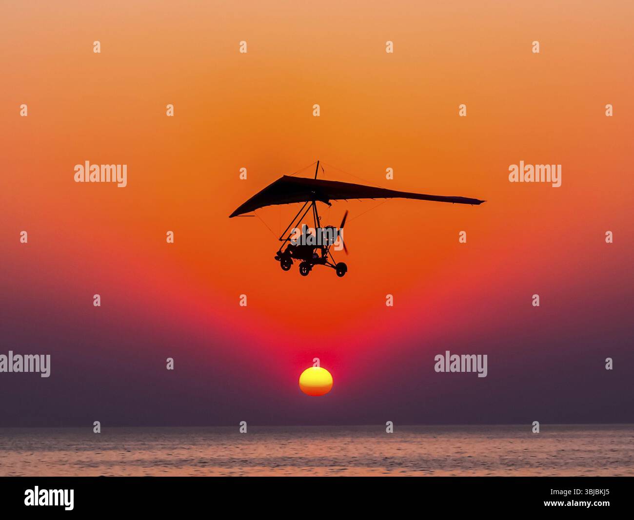 Die Person, die auf einem Dreirad mit dem Motor gegen den Drachenflieger fliegt, fliegt gegen den Sonnenuntergang Stockfoto