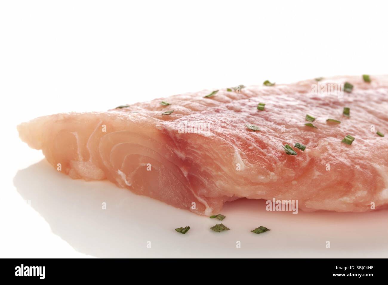 Gefrorenes Fischfilet mit frischen grünen Kräutern, isoliert auf weißem Hintergrund. Kulinarische Meeresfrüchte Stockfoto