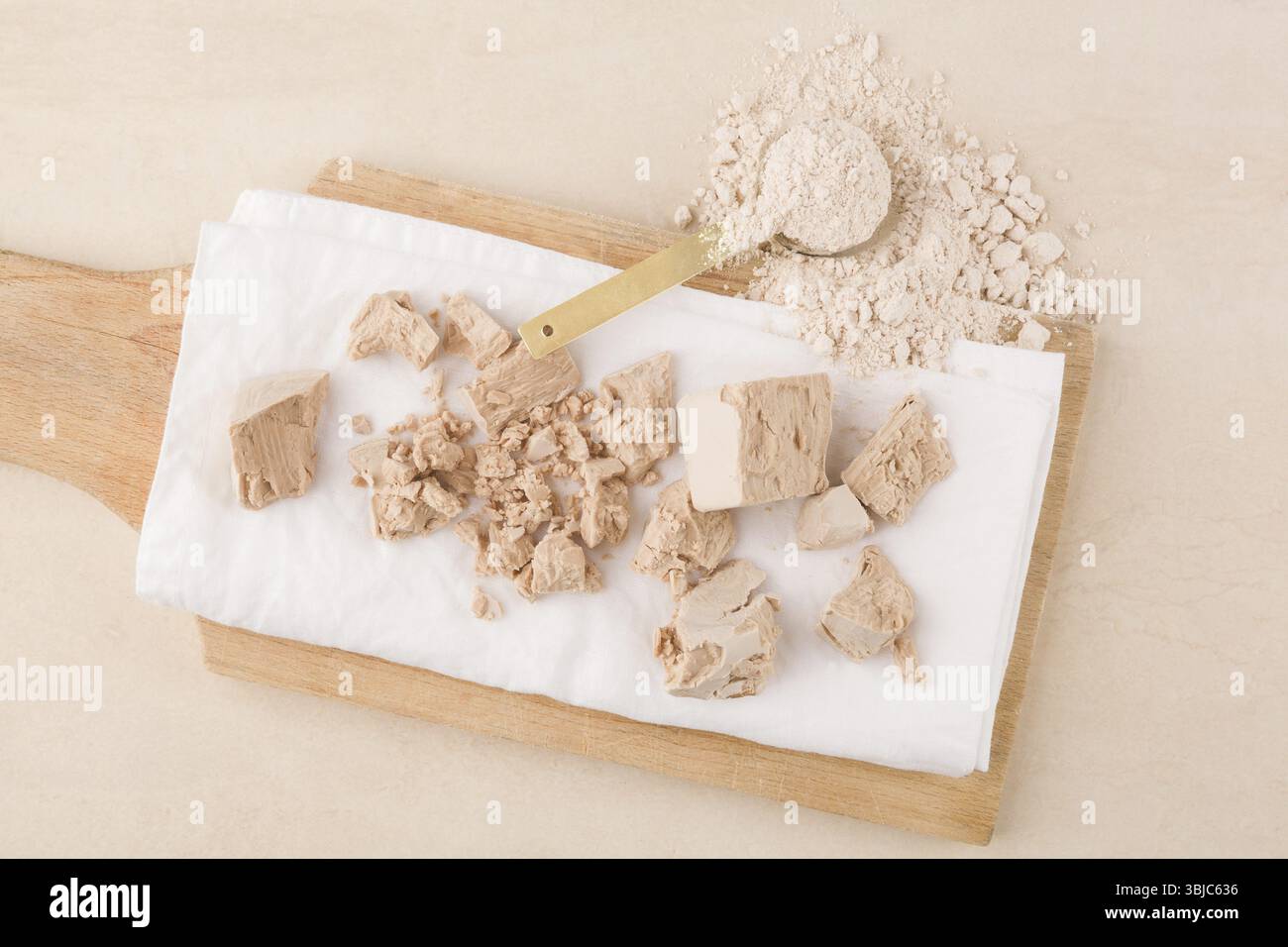 Teigherstellung. Hefeblöcke und Mehl auf Holzbrett auf beigefarbenem Hintergrund Stockfoto