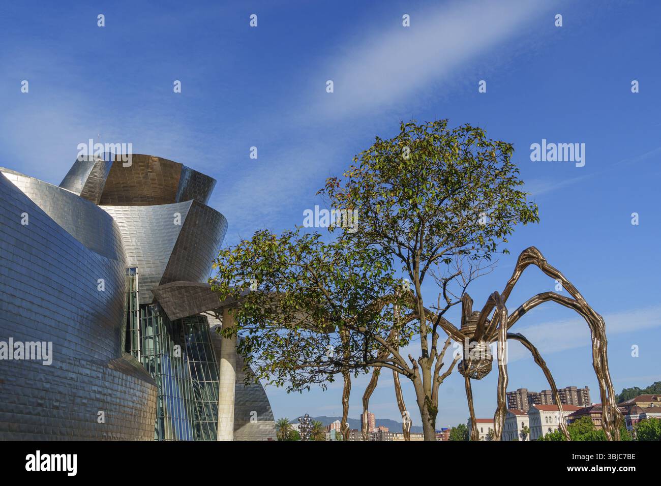 Große Spinnenskulptur neben Metallbau und Baum unter blauem Himmel, Bilbao, Baskenland, Spanien, Europa Stockfoto