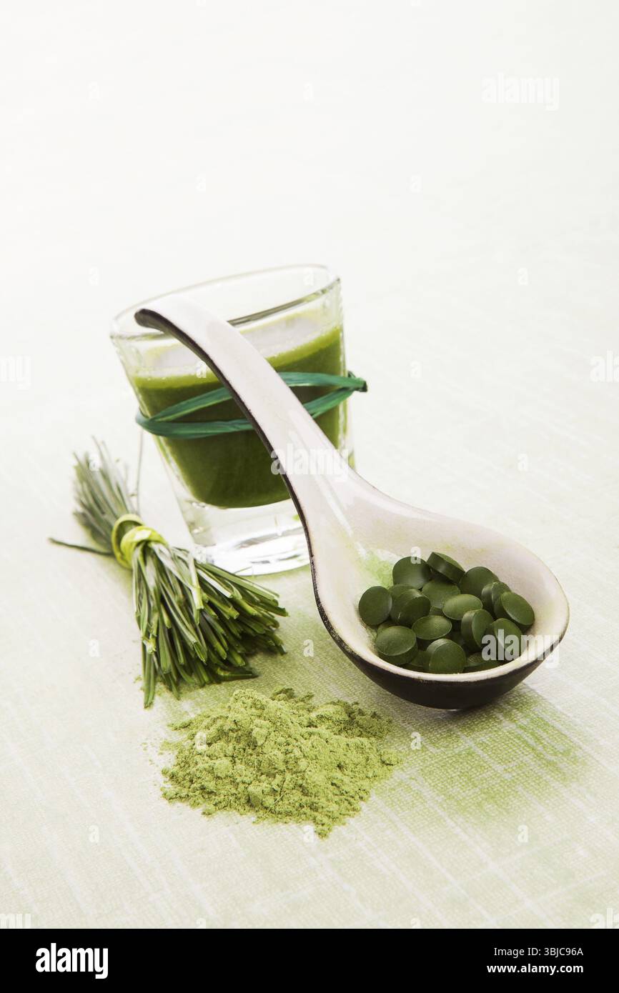 Weizengras, Gerstengras, Chlorella, Spirulina. Pflanzliche natürliche Nahrungsergänzungsmittel. Gemahlenes Pulver, Pillen auf dem Löffel und grüner Saft Stockfoto