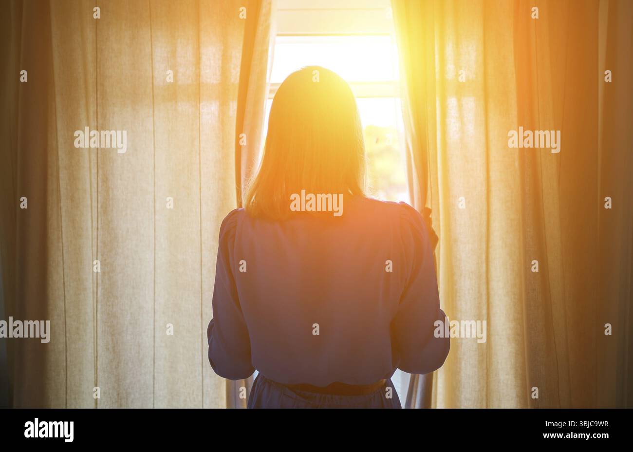 Frau, die am sonnigen Morgen Vorhänge im Zimmer öffnet Stockfoto