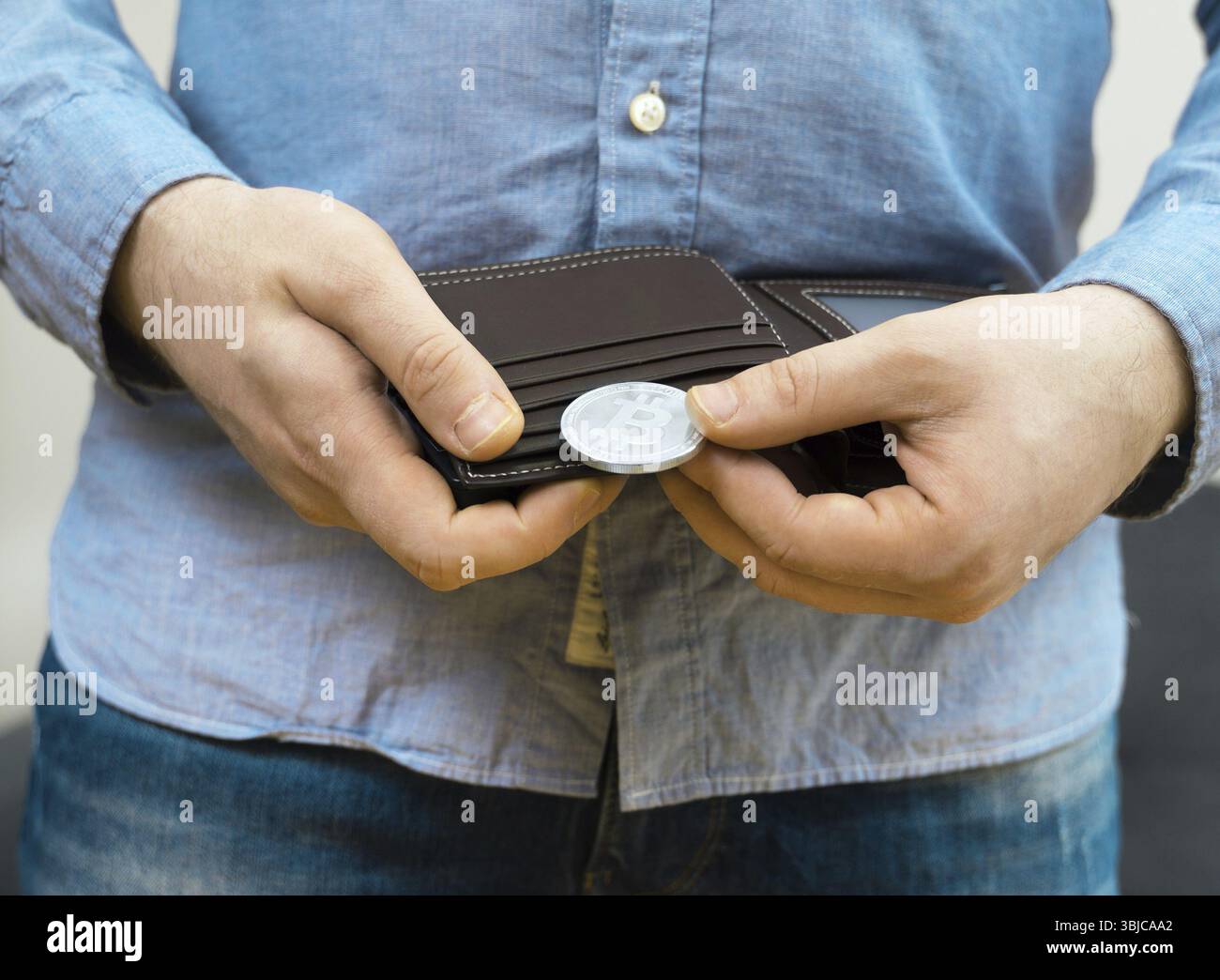 Mann mit einer physischen Version von silbernem Bitcoin Stockfoto