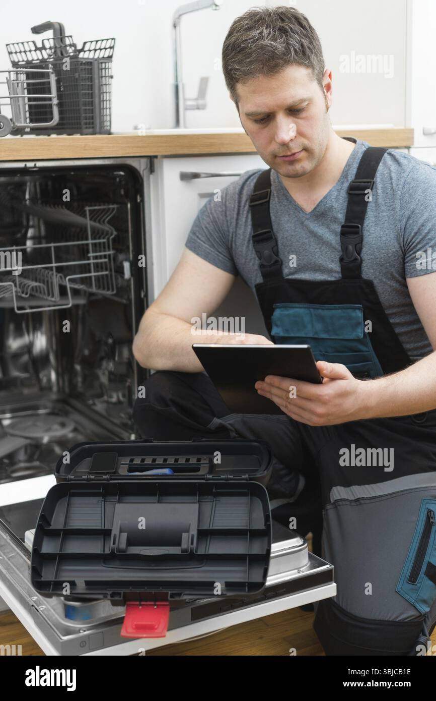 Handwerker mit Tablet-pc, der Haushaltsspülmaschine in der Küche repariert Stockfoto