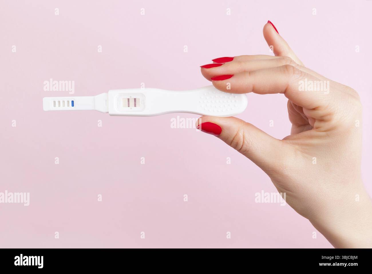 Schöne weibliche Hand mit roten Fingernägeln Holding positiven Schwangerschaftstest auf rosa Hintergrund isoliert. Mutterschaft, Schwangerschaft, Geburt Steuerungskonzept. Stockfoto